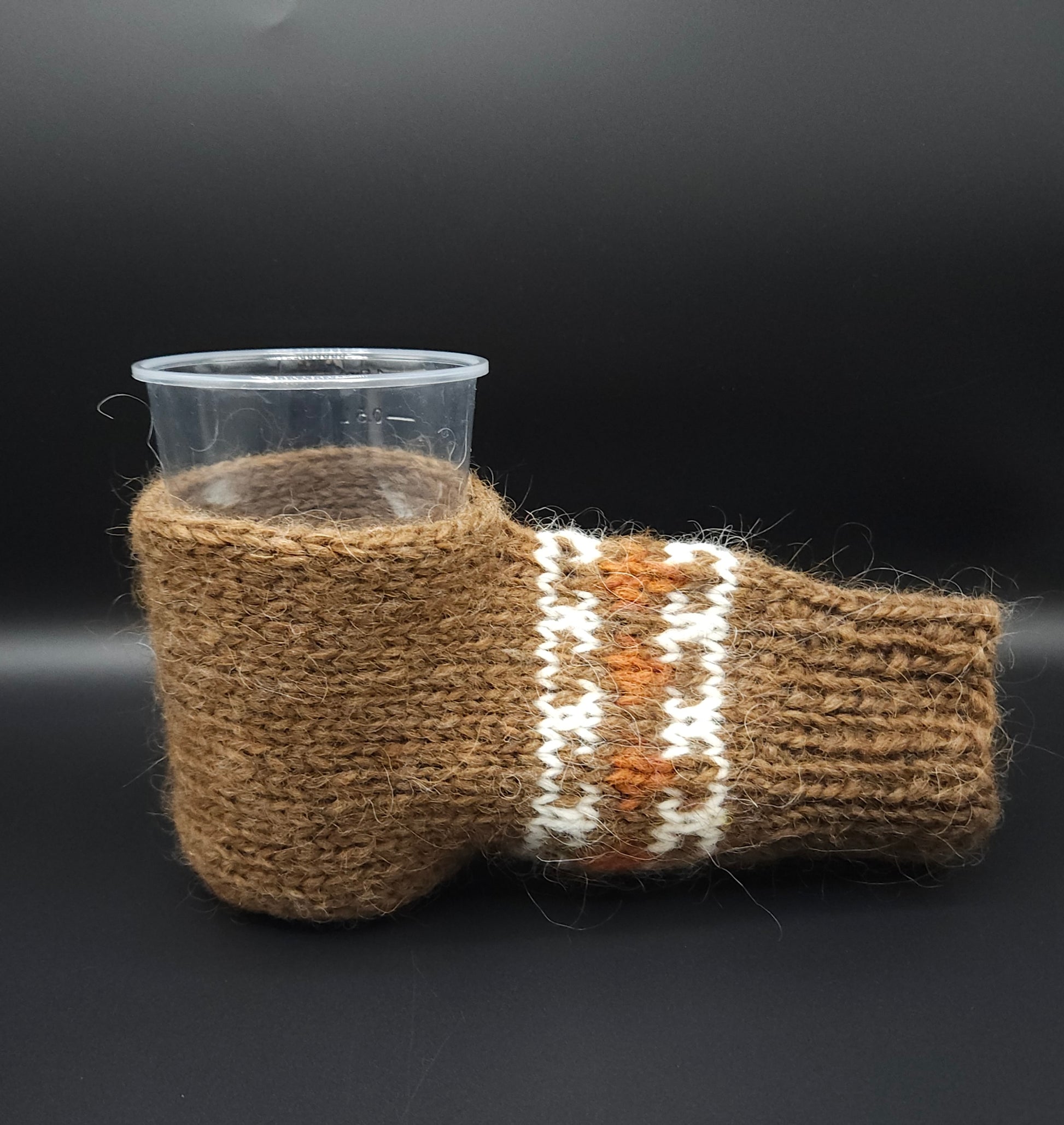 Brown knitted mitten for holding beer with a pattern on a black background