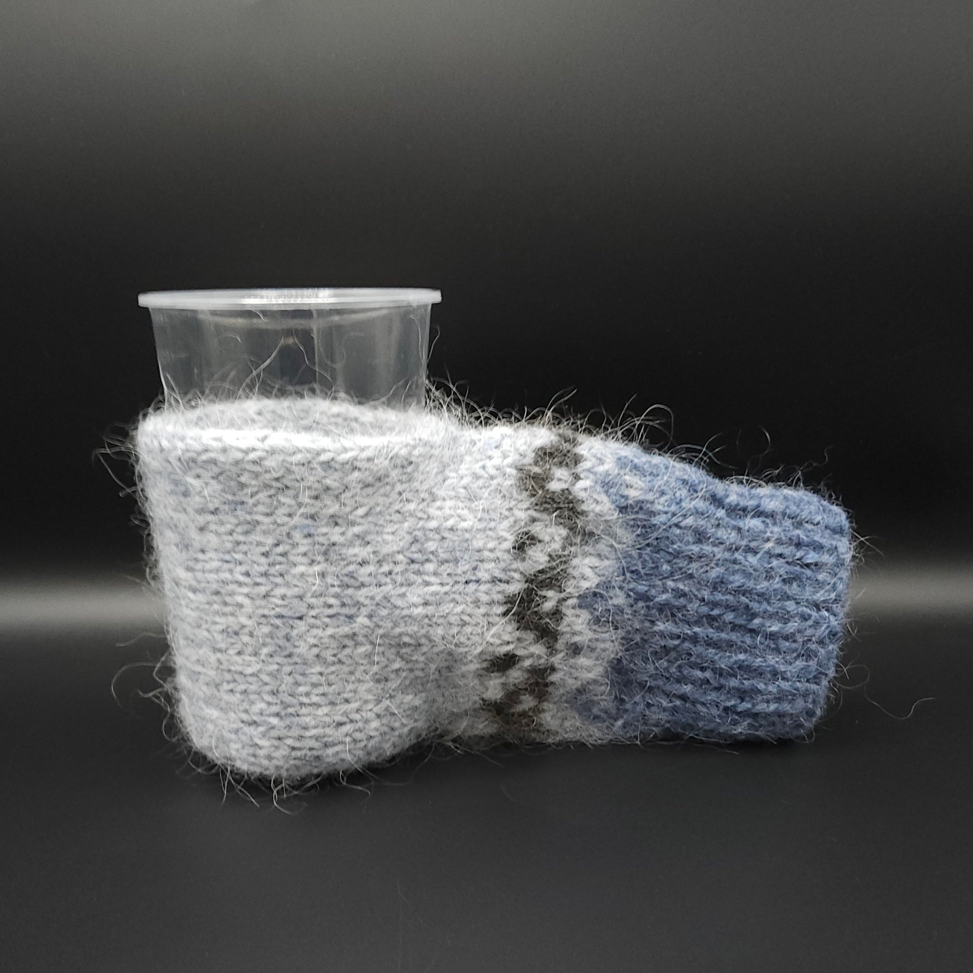 Knitted mitten for holding beer in light blue and darker blue on a black background