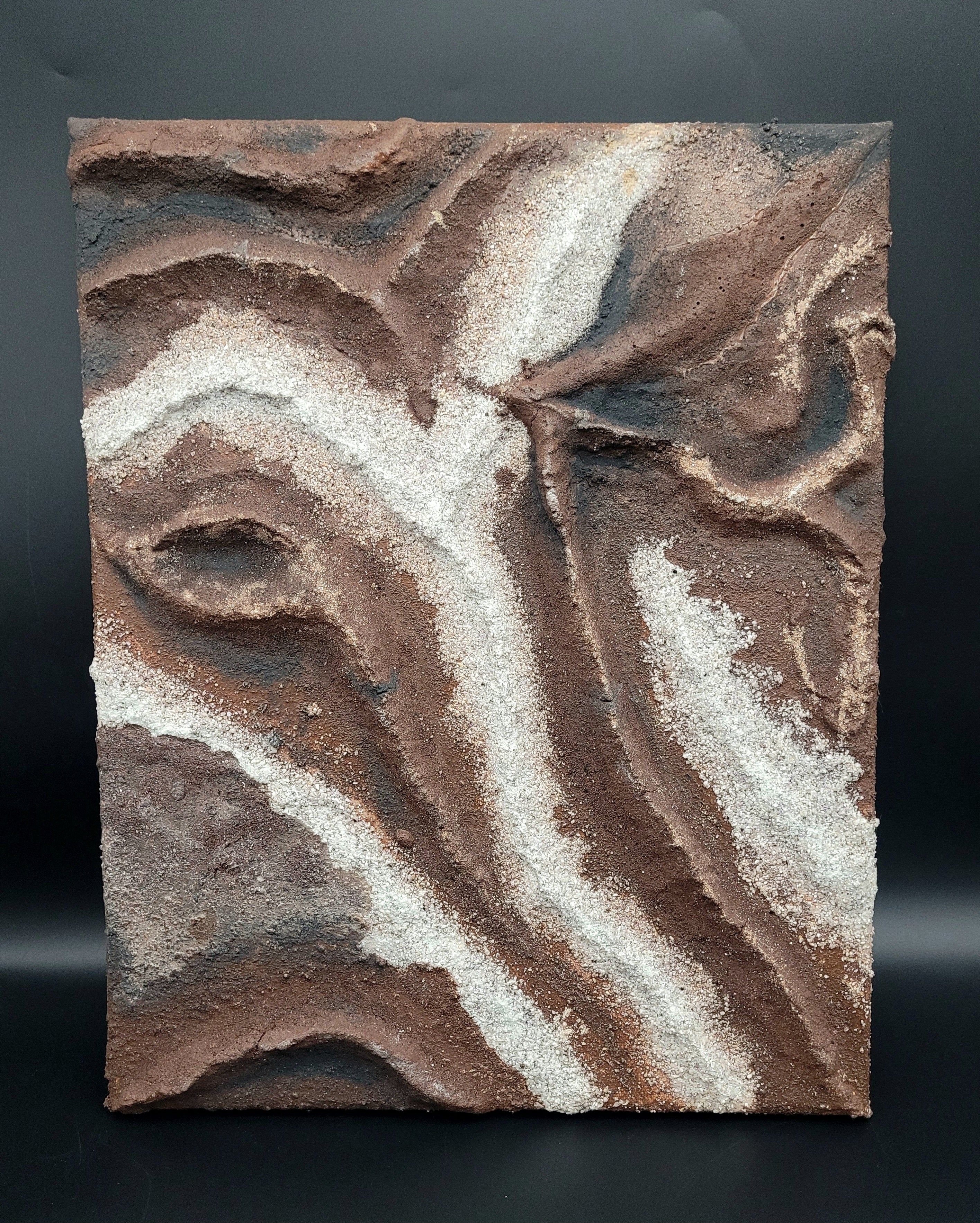 Textured wall art with brown and beige patterns on a black background