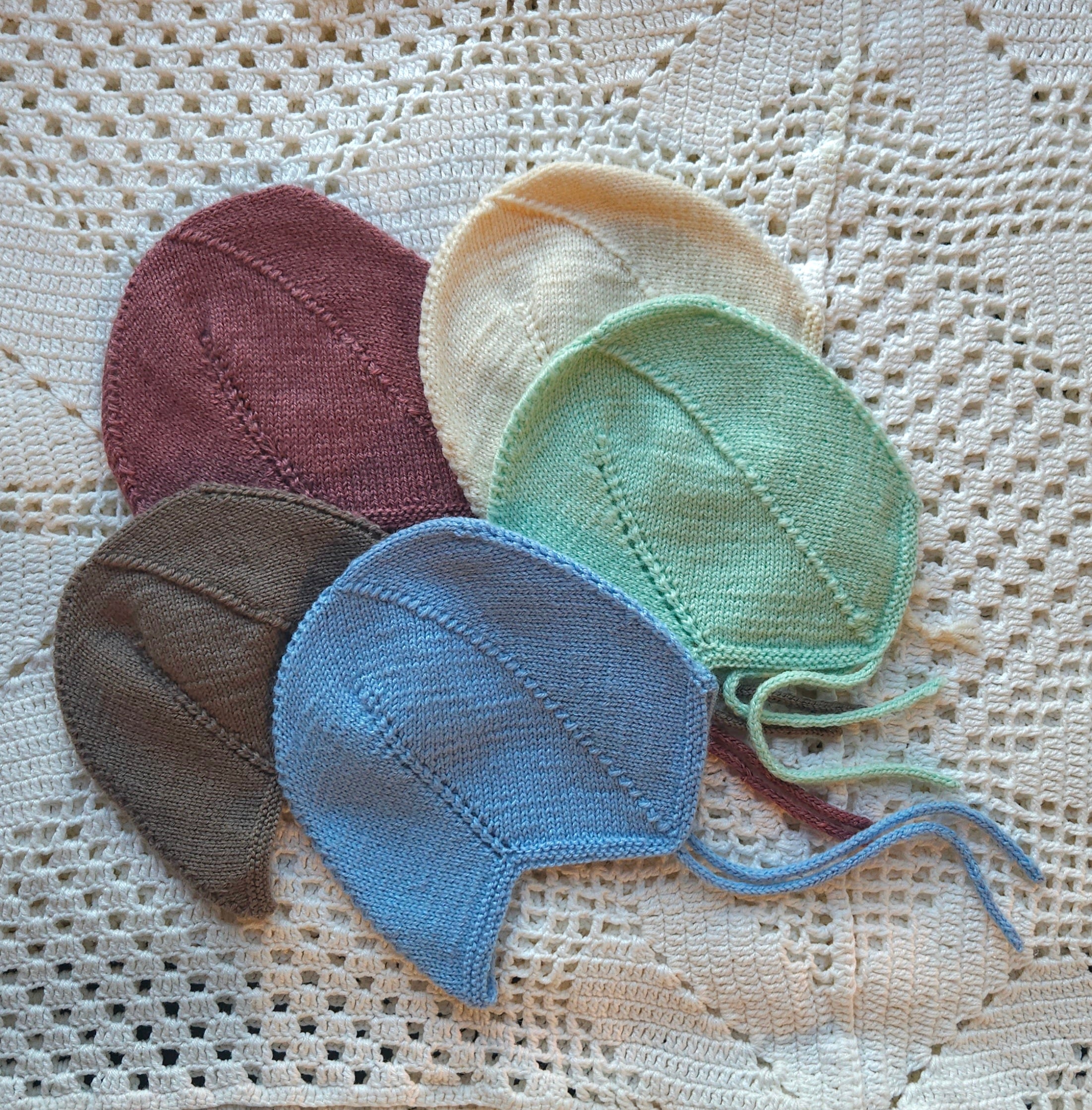 Four knitted baby hats in different colors on a textured fabric background