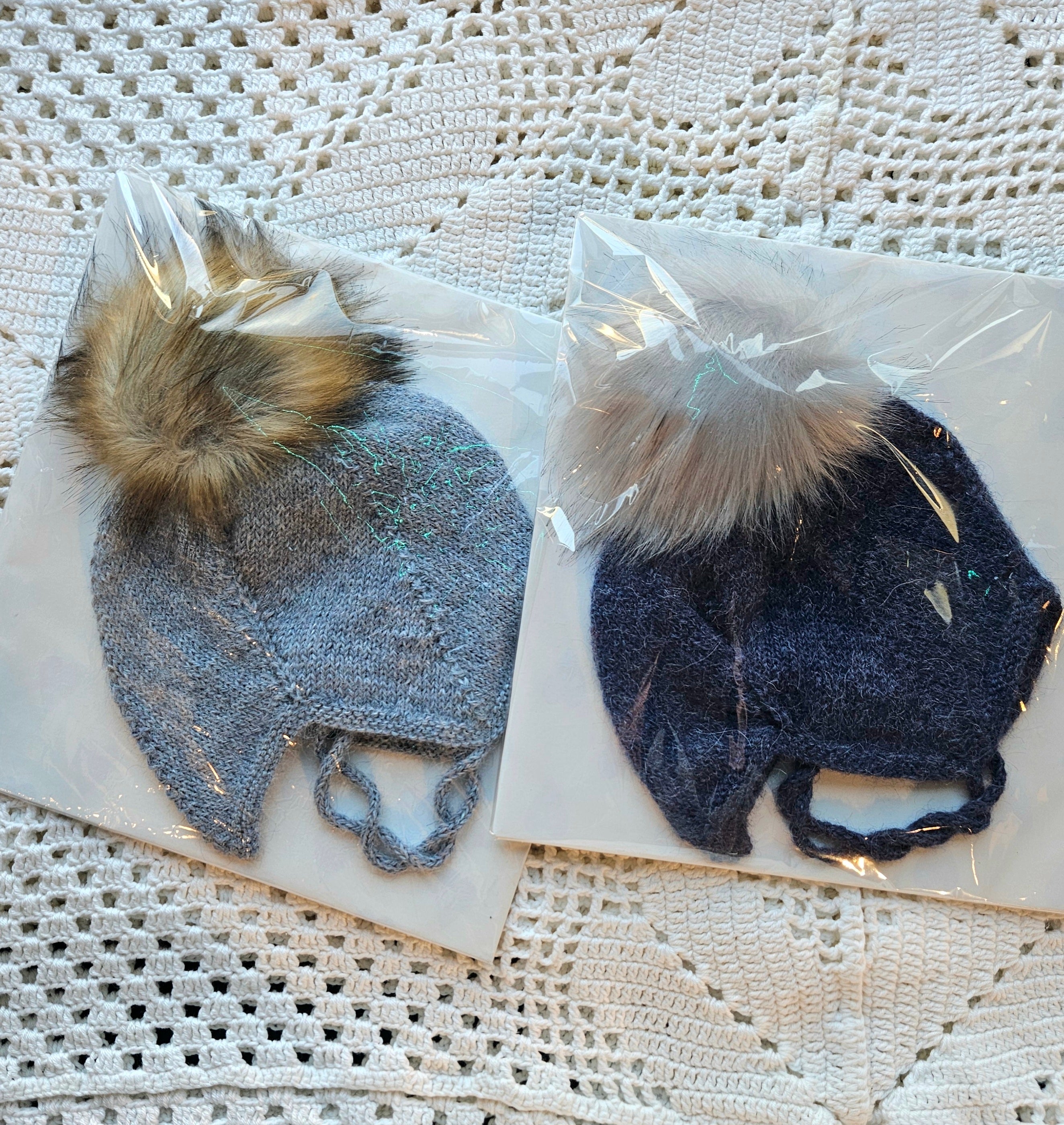 Two knitted hats with fur pom-poms on a textured surface