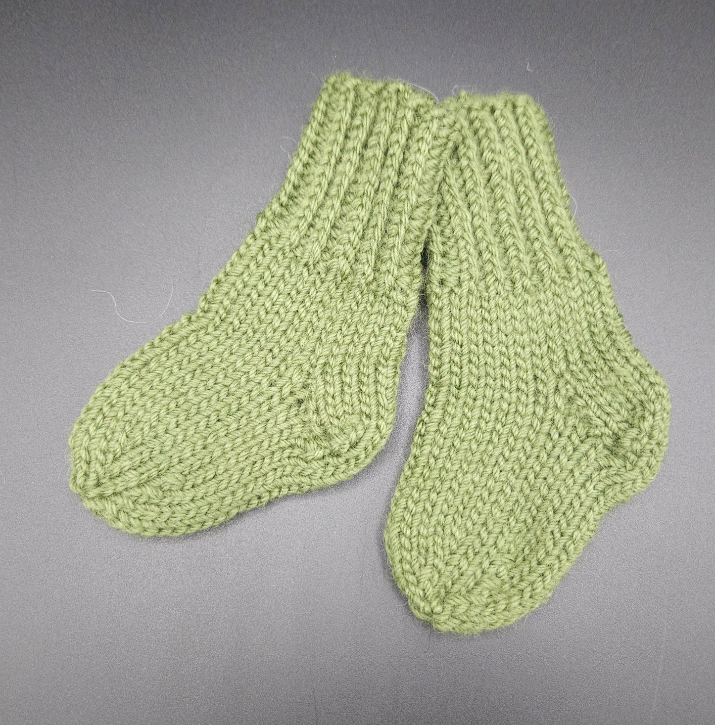 Pair of green knitted socks on a gray background