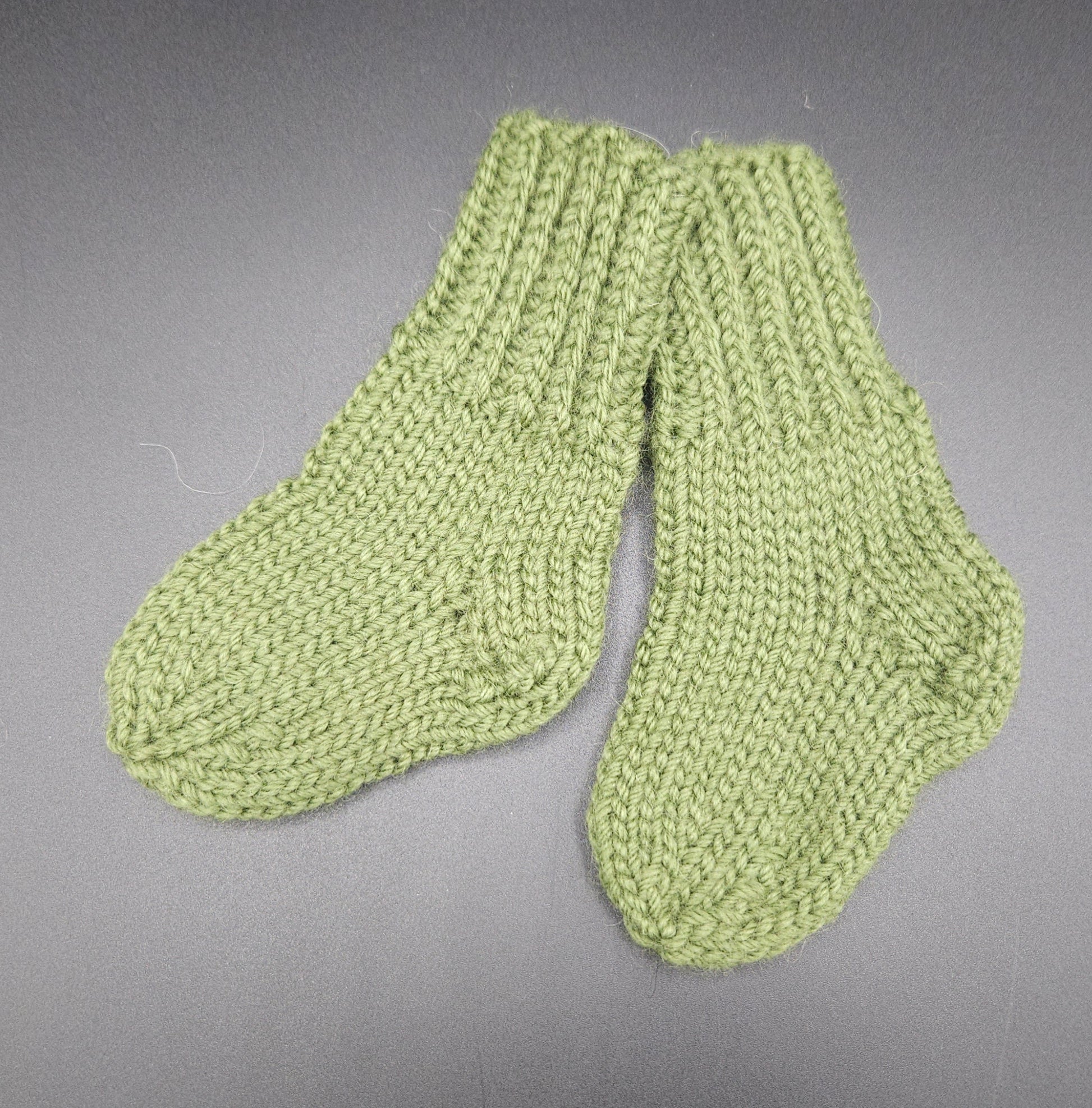 Pair of green knitted socks on a gray background