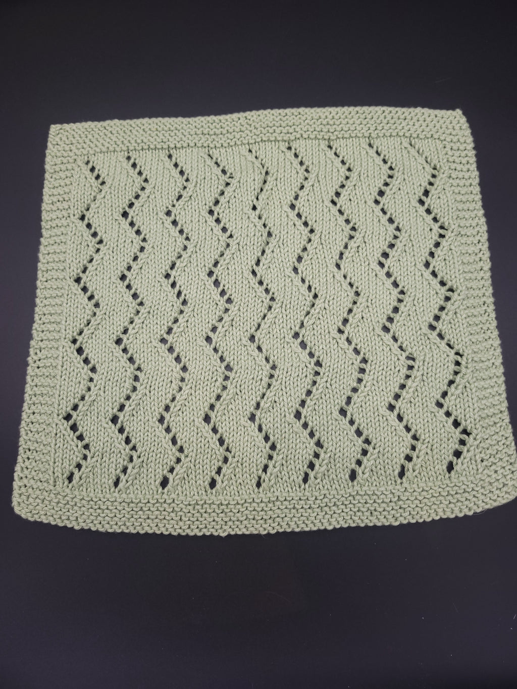 Knitted washcloth in green with a zigzag pattern on a dark background