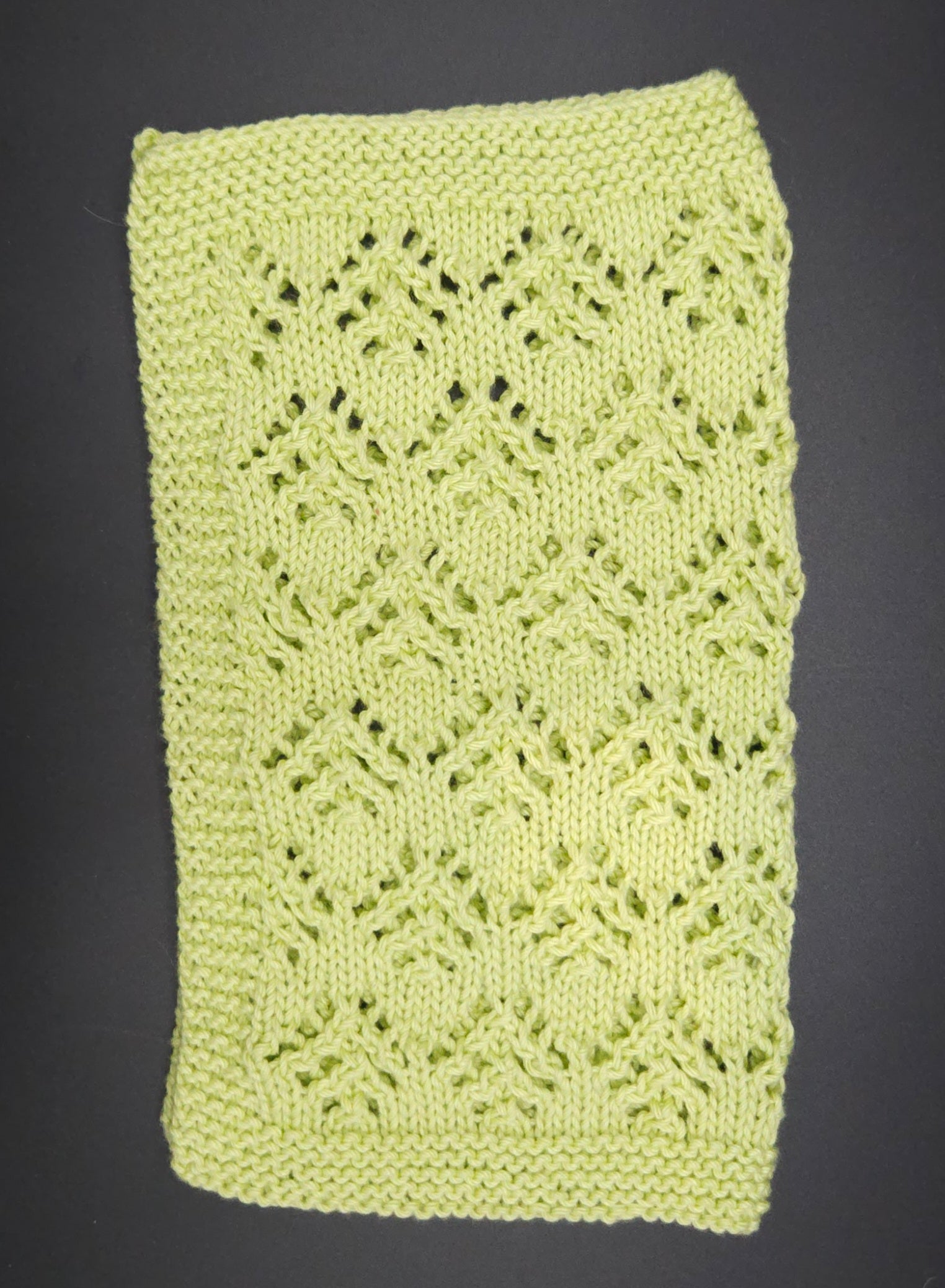 Green knitted washcloth with a lace pattern on a dark background