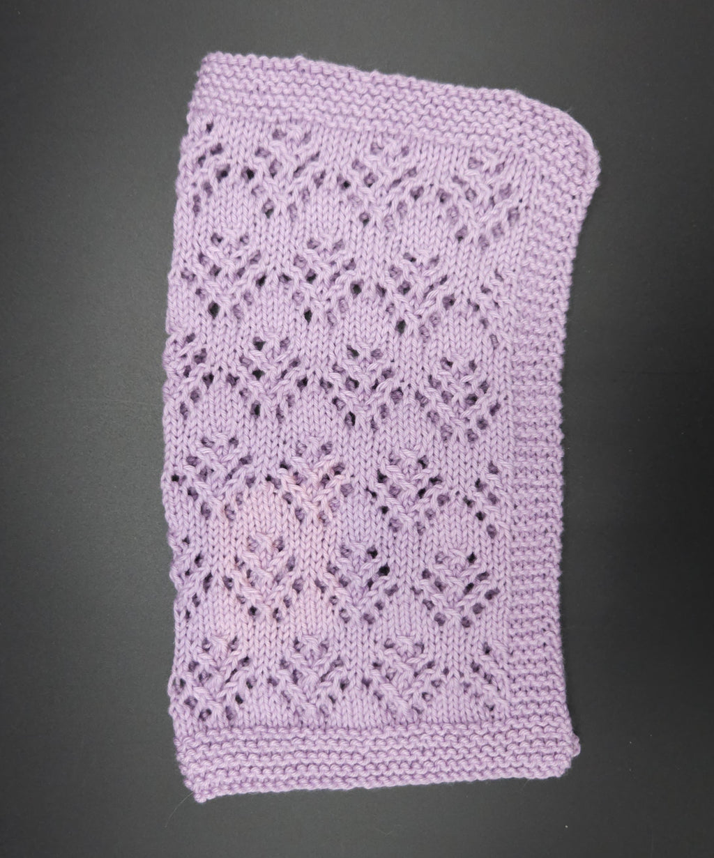 Purple knitted washcloth with a lace pattern on a black background