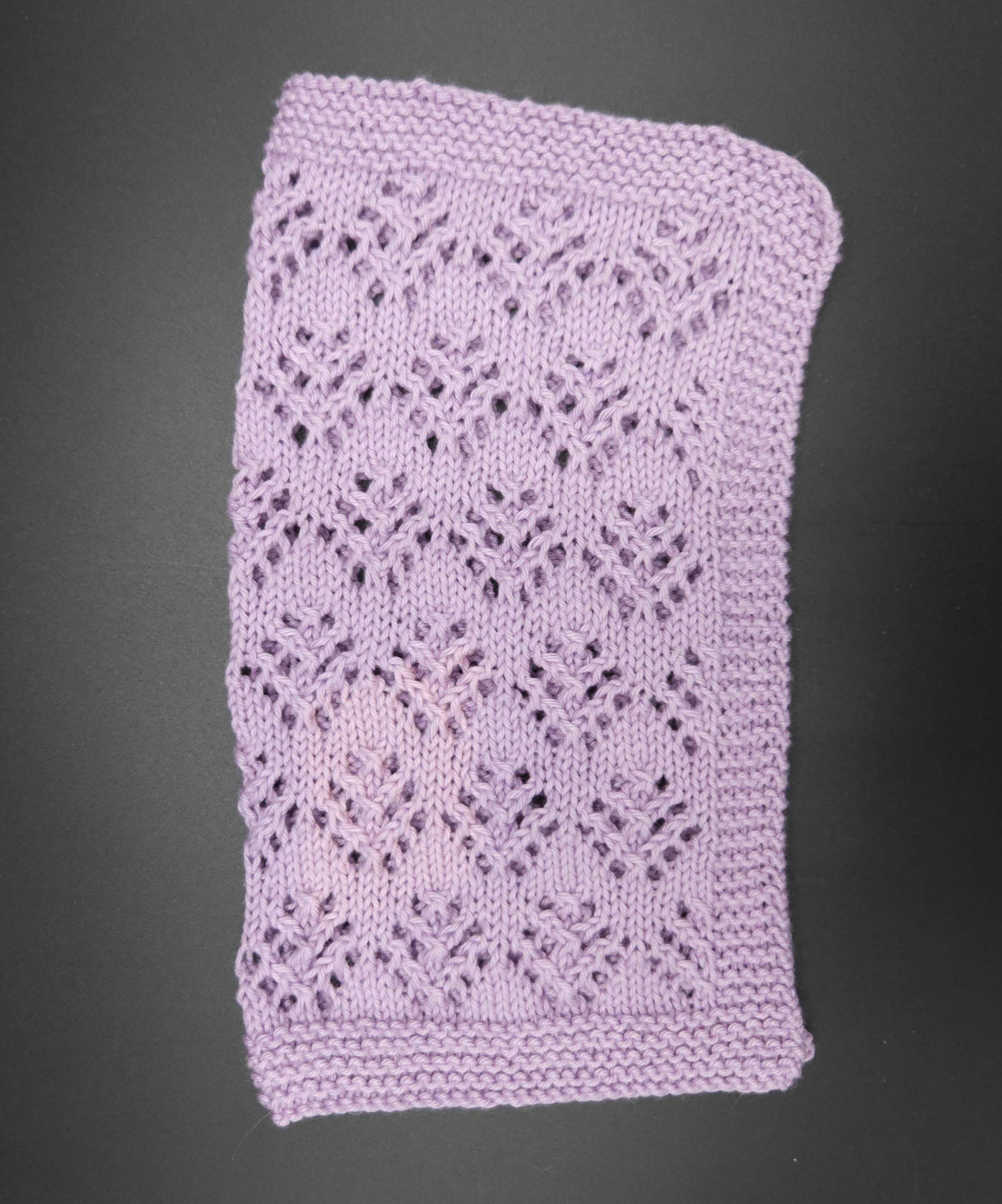 Purple knitted washcloth with a lace pattern on a black background