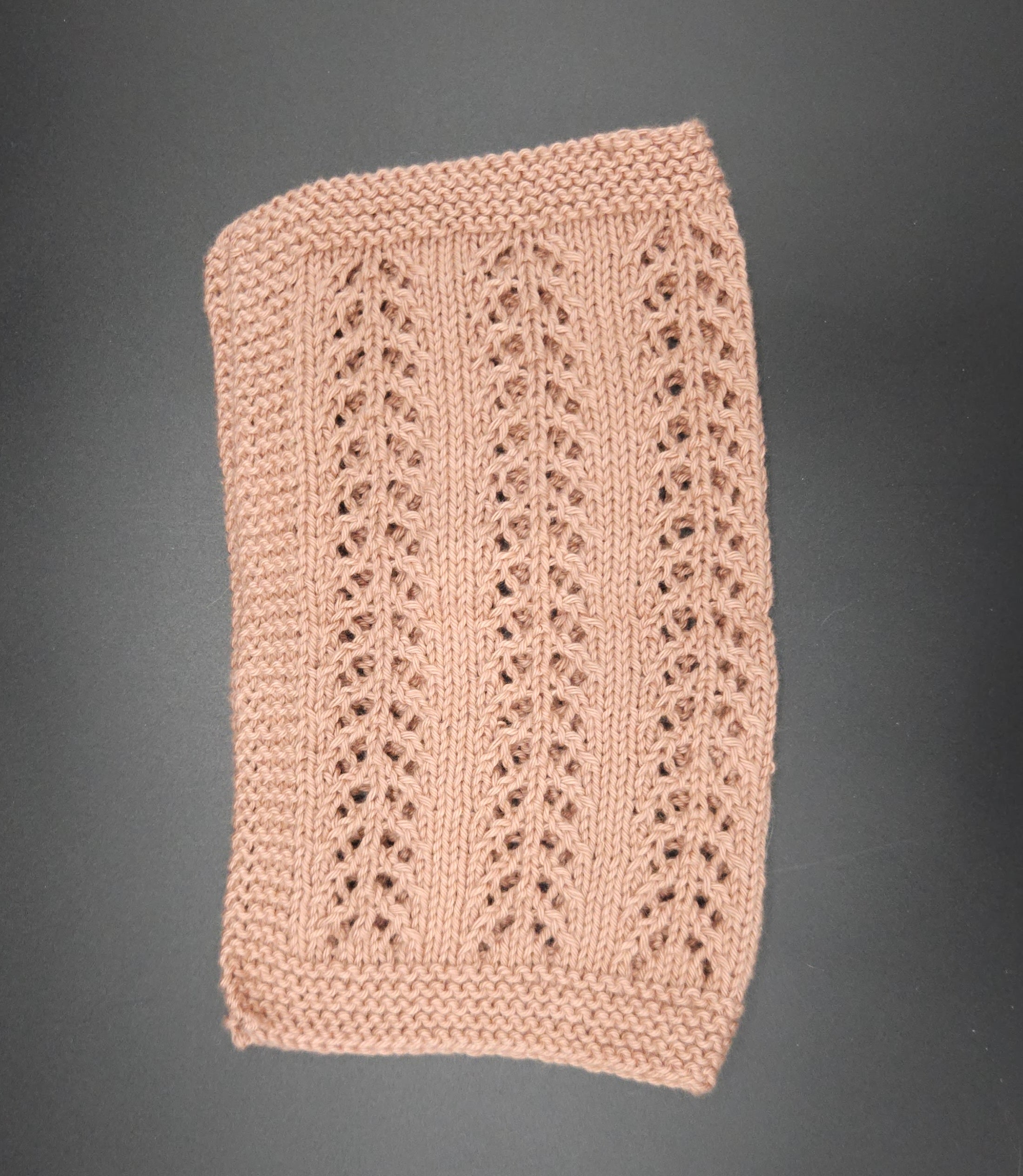 Beige knitted washcloth with a textured pattern on a dark gray background