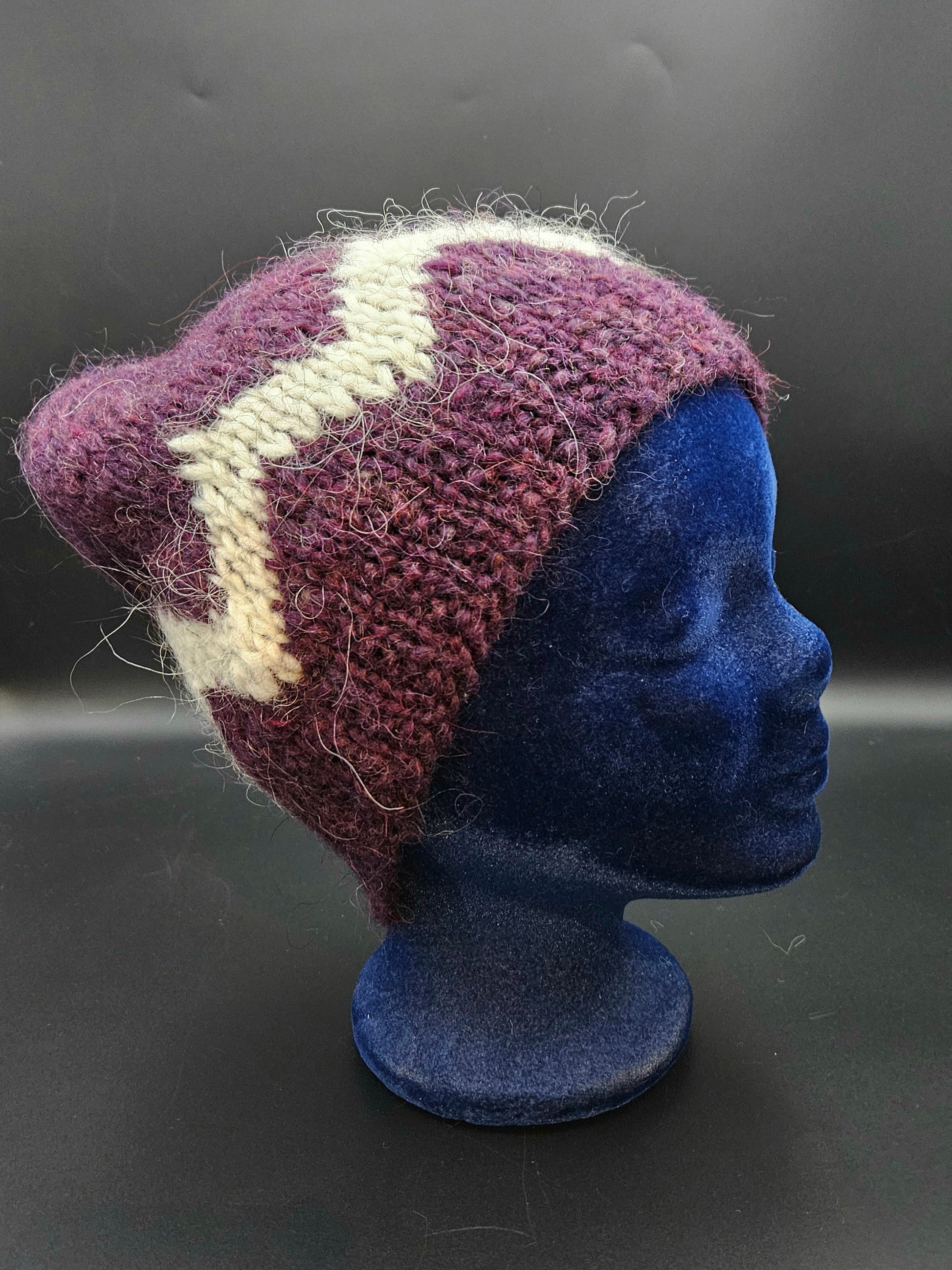 Knitted hat with purple and white pattern on a mannequin head against a dark background