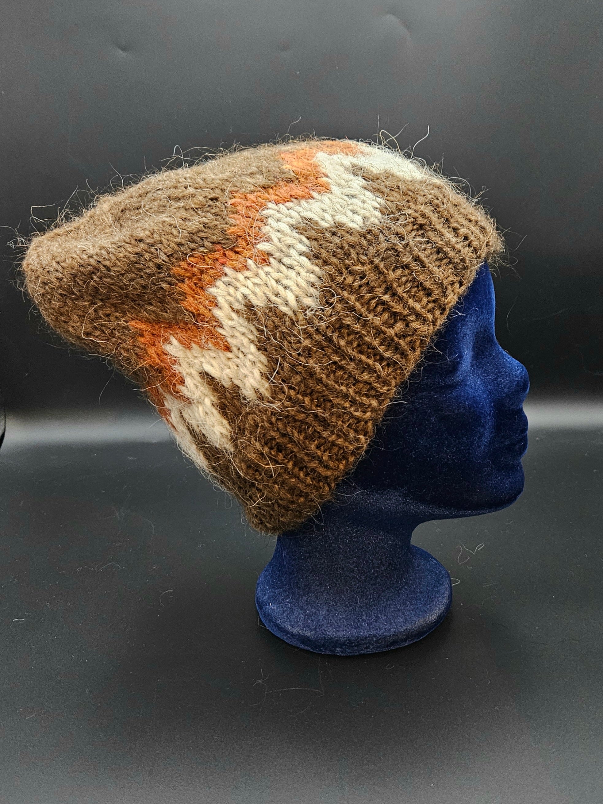 Knitted hat with brown, orange, and white pattern on a blue mannequin head against a dark background