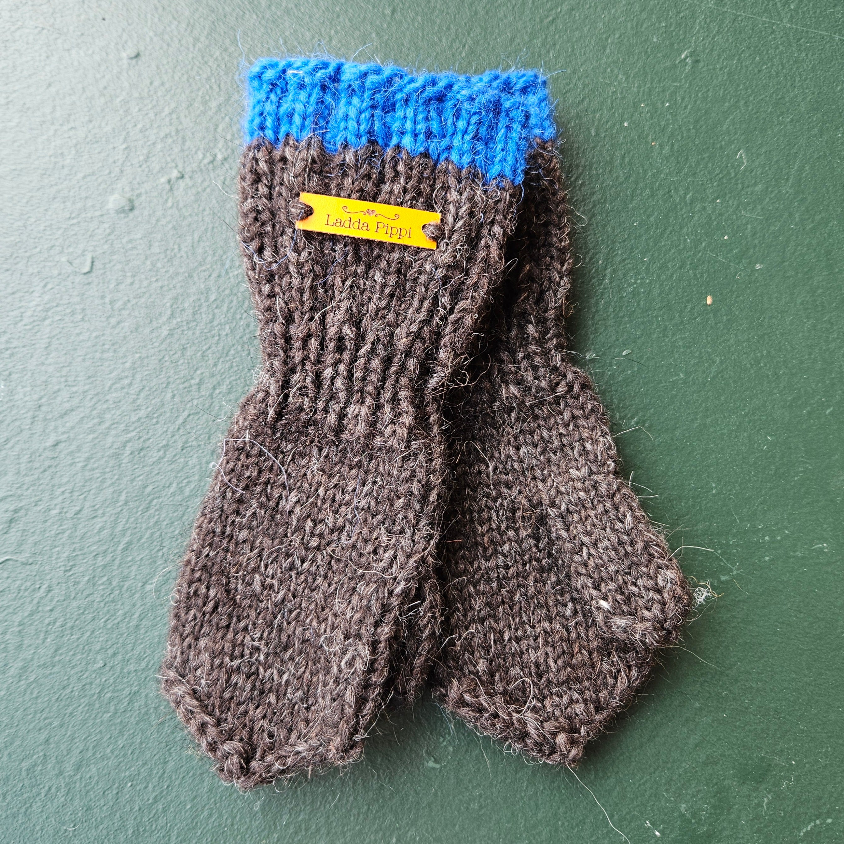 Pair of black knitted mittens with blue cuff on a green background