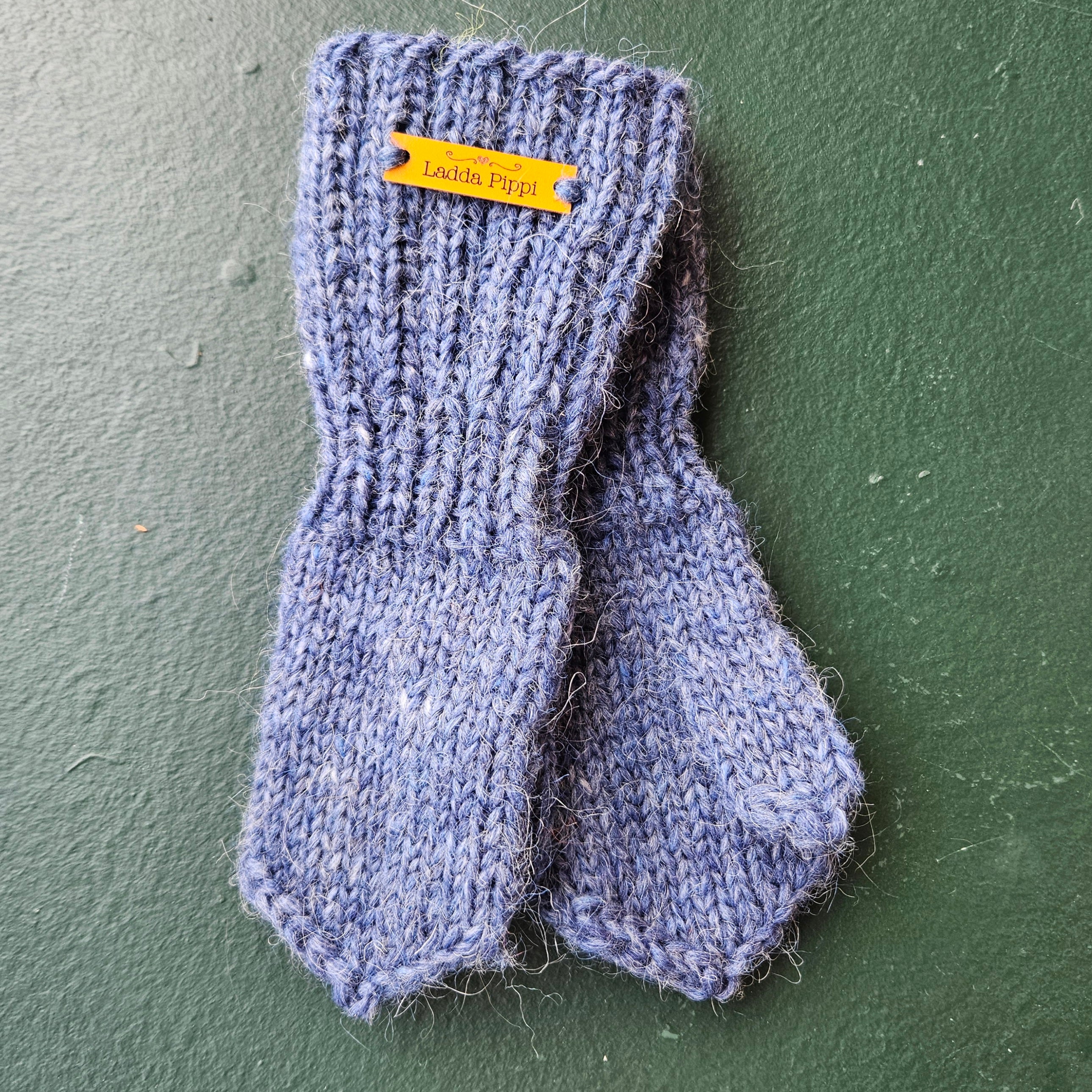 Pair of blue knitted mittens with a label on a green background