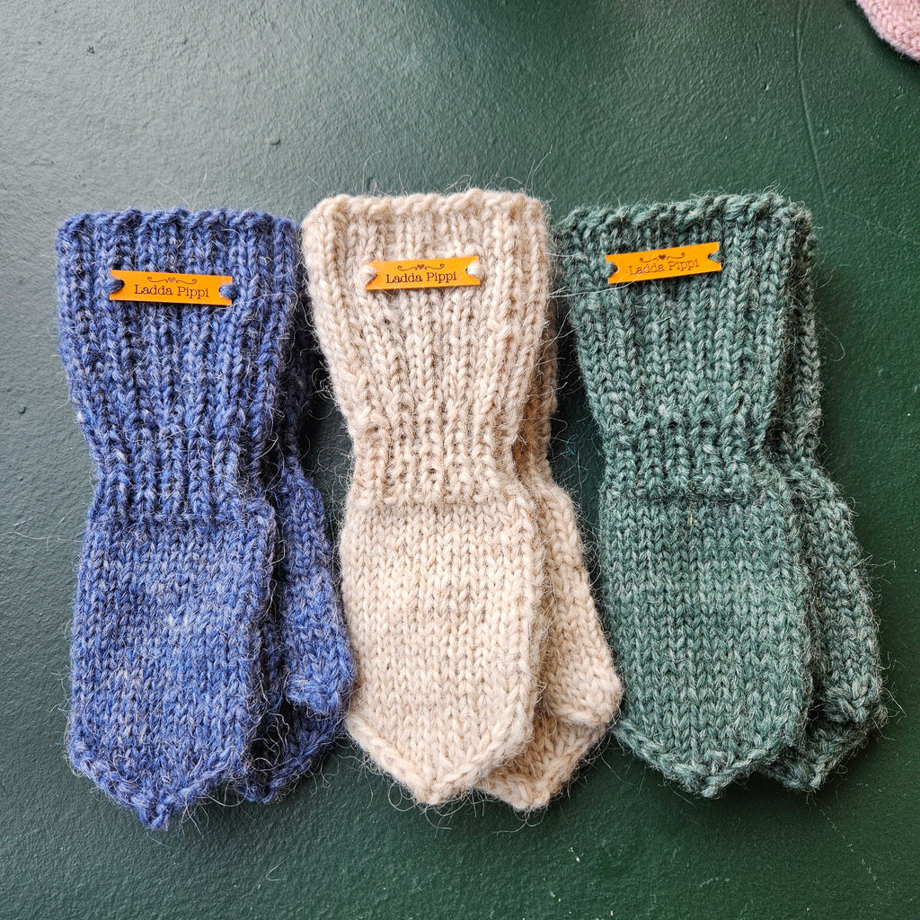 Three pairs of knitted mittens in green, beige, and blue on a dark surface.