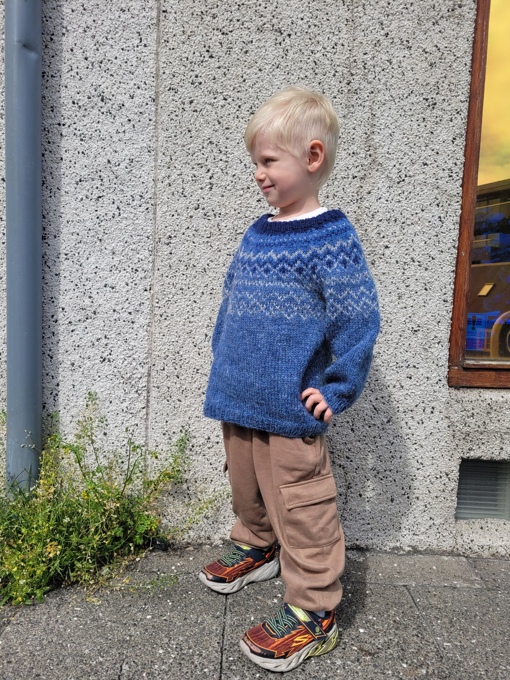 Child wearing a blue hand-knit Icelandic wool sweater featuring a traditional Nordic pattern