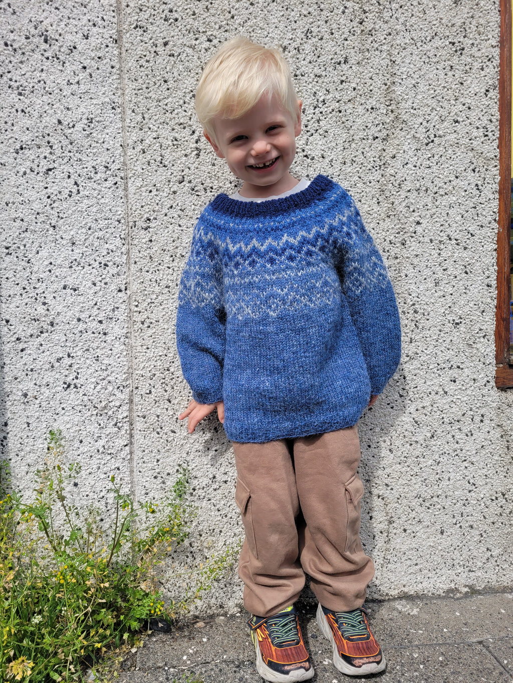 Child wearing a blue hand-knit Icelandic wool sweater featuring a traditional Nordic pattern