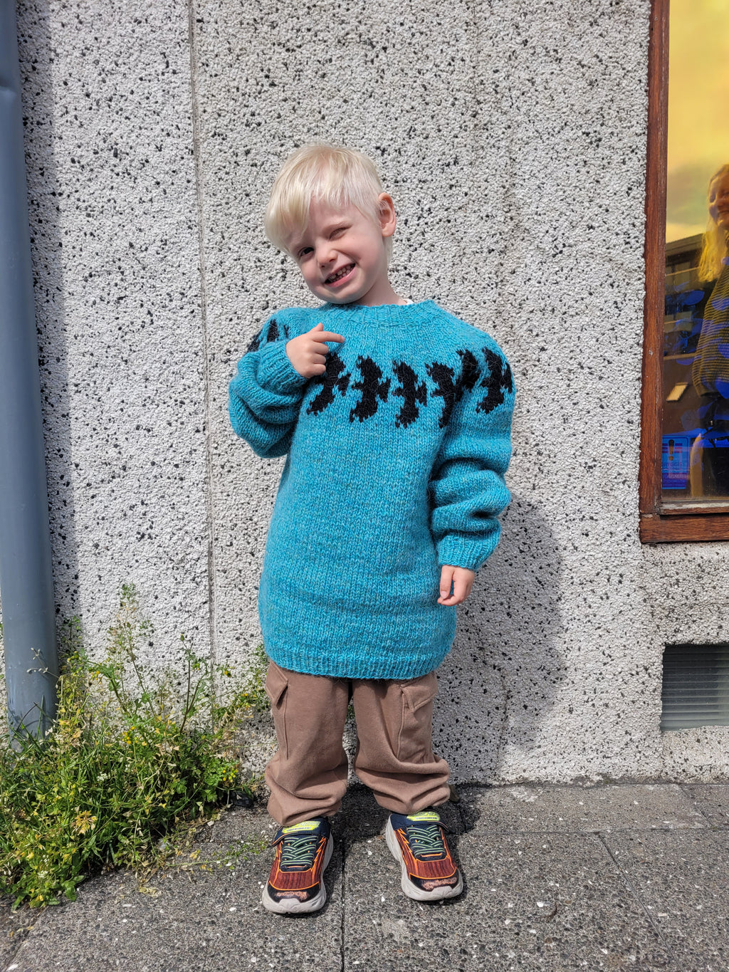 Child wearing a blue sweater with black patterned ravens standing on a street corner.