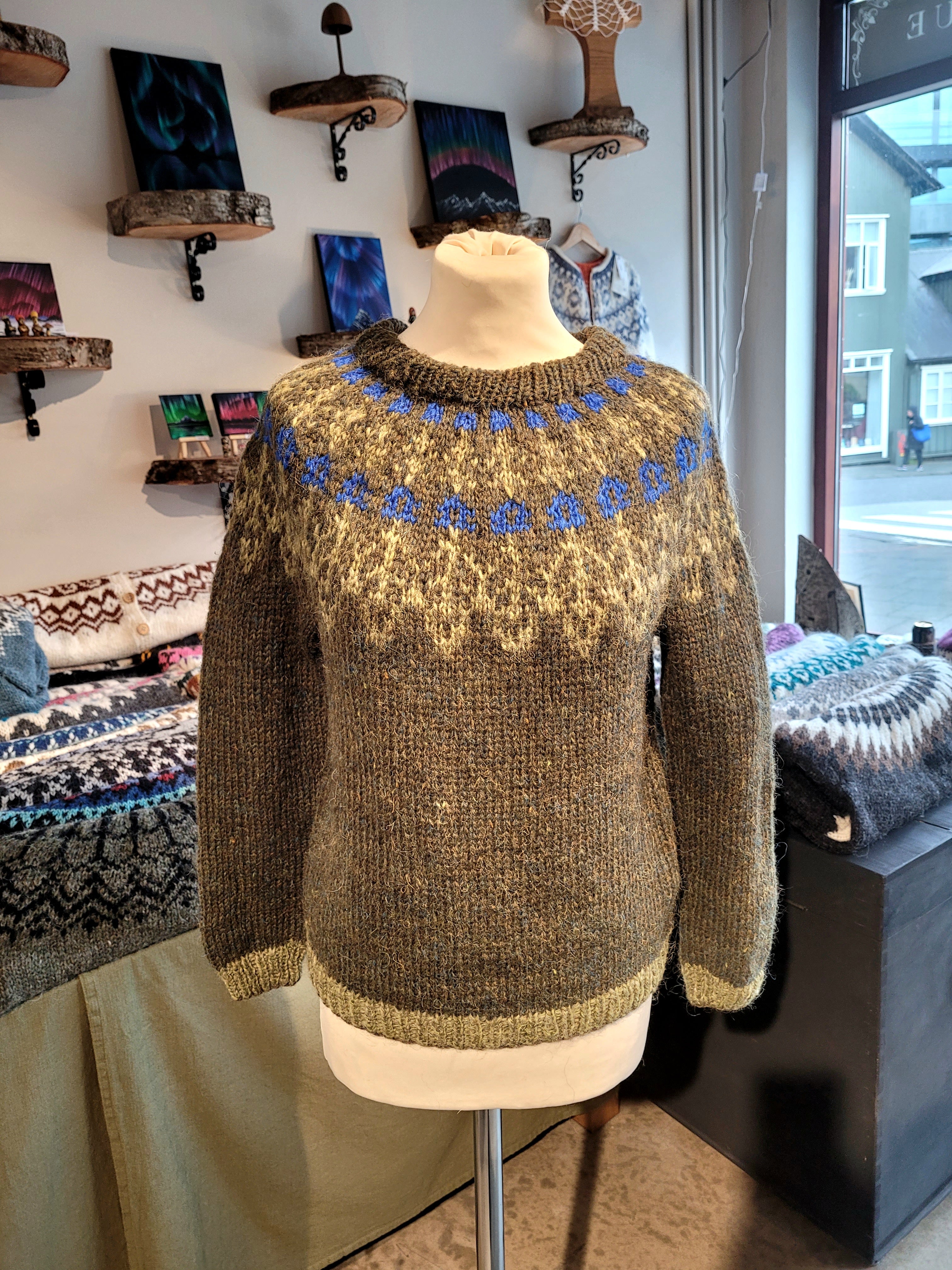 Green hand-knit Icelandic wool sweater featuring a traditional Nordic pattern in  light green and blue colors on a mannequin in a store setting