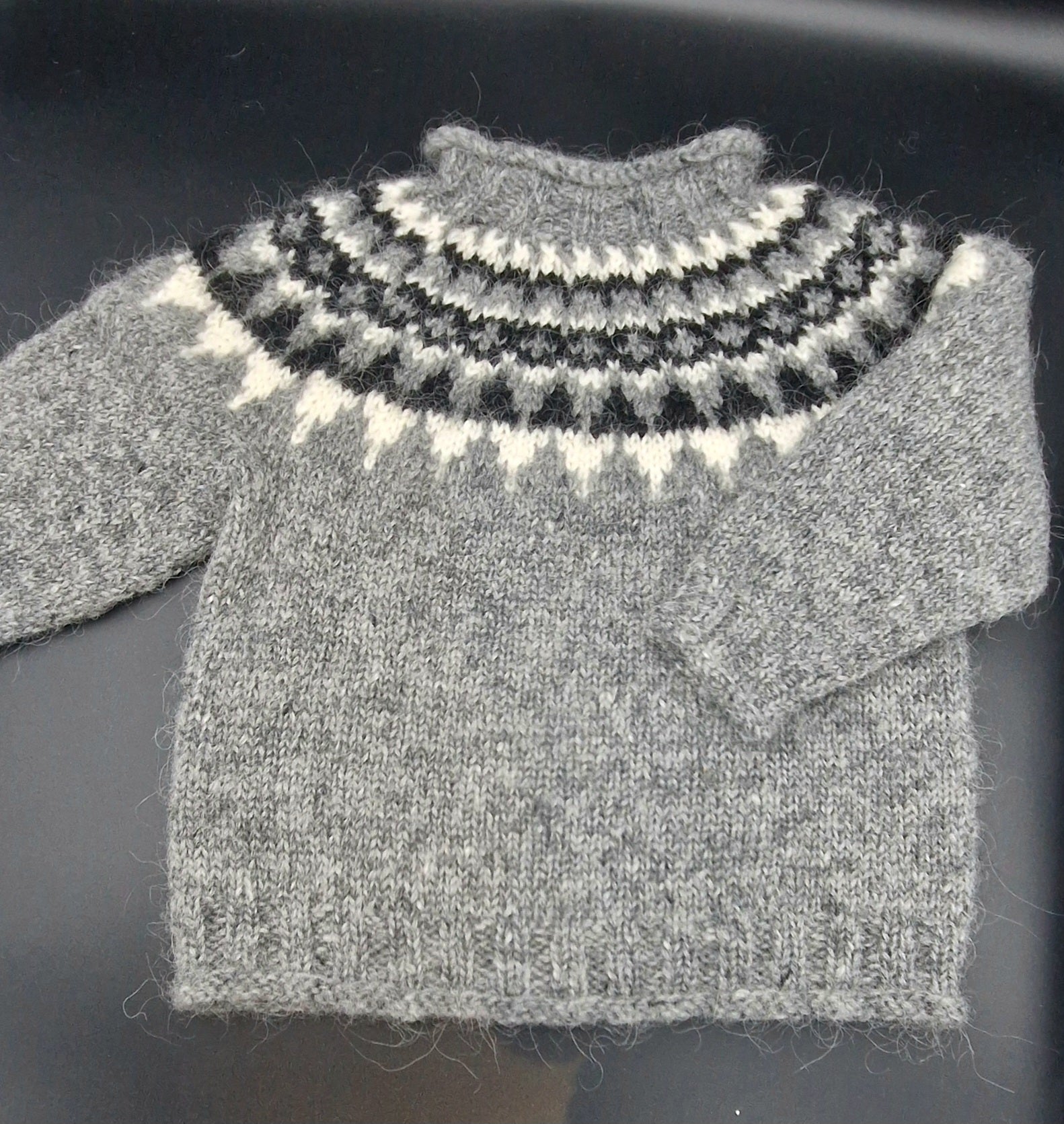 Gray hand-knit Icelandic wool sweater featuring a traditional Nordic pattern in  white and black colors on a black surface