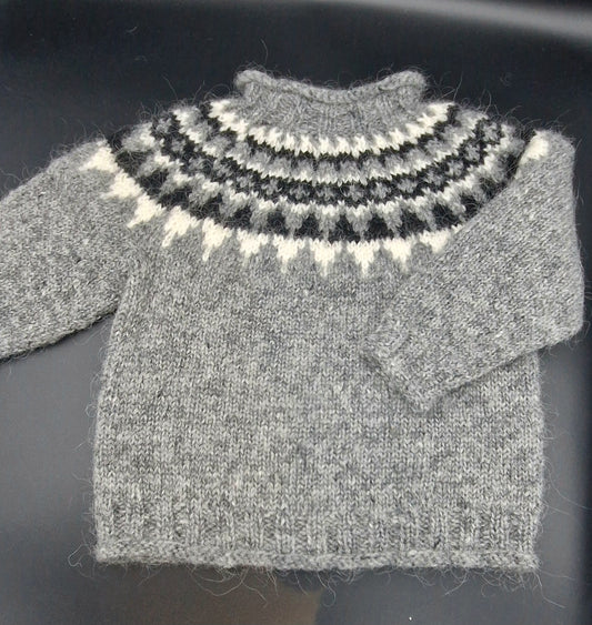 Gray hand-knit Icelandic wool sweater featuring a traditional Nordic pattern in  white and black colors on a black surface