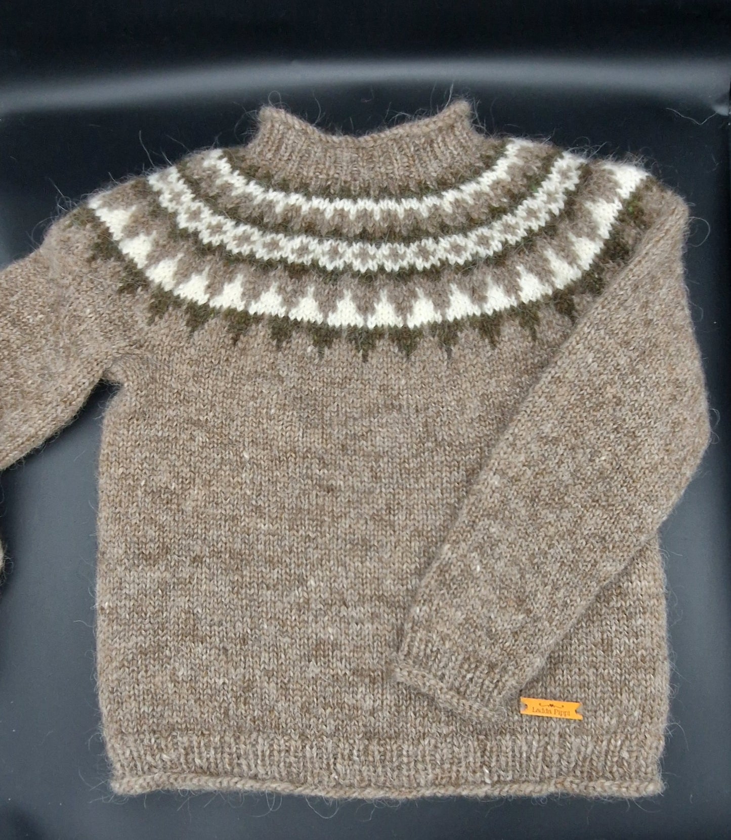 Light brown hand-knit Icelandic wool sweater featuring a traditional Nordic pattern in brown, white, and beige colors on a black surface