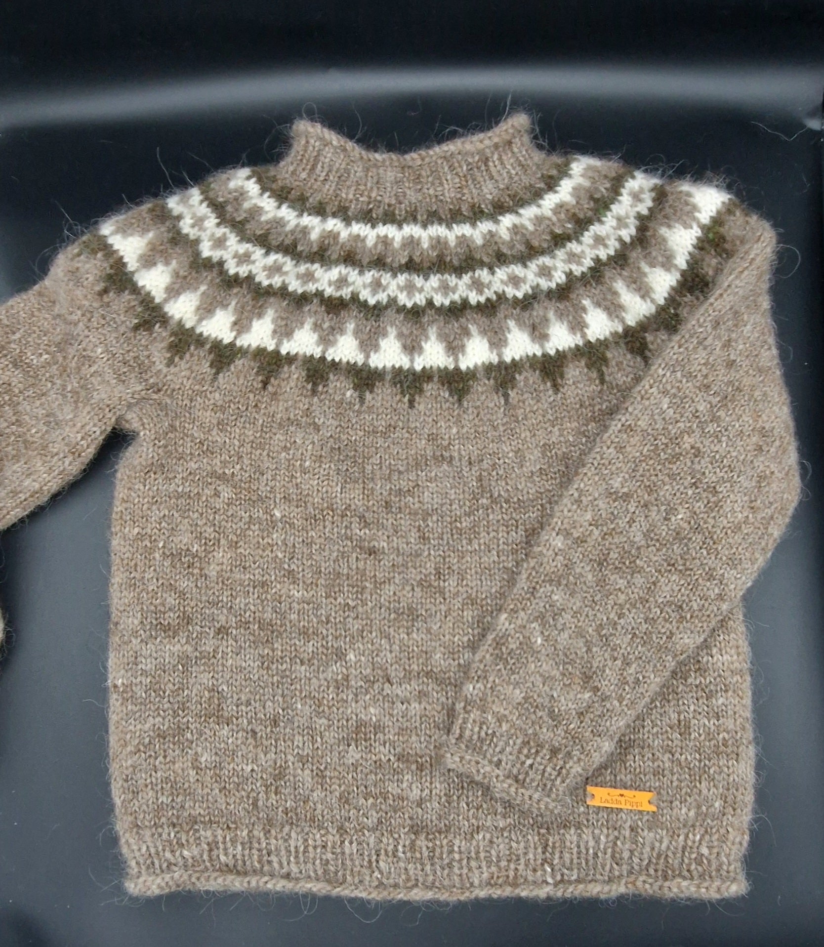 Light brown hand-knit Icelandic wool sweater featuring a traditional Nordic pattern in brown, white, and beige colors on a black surface