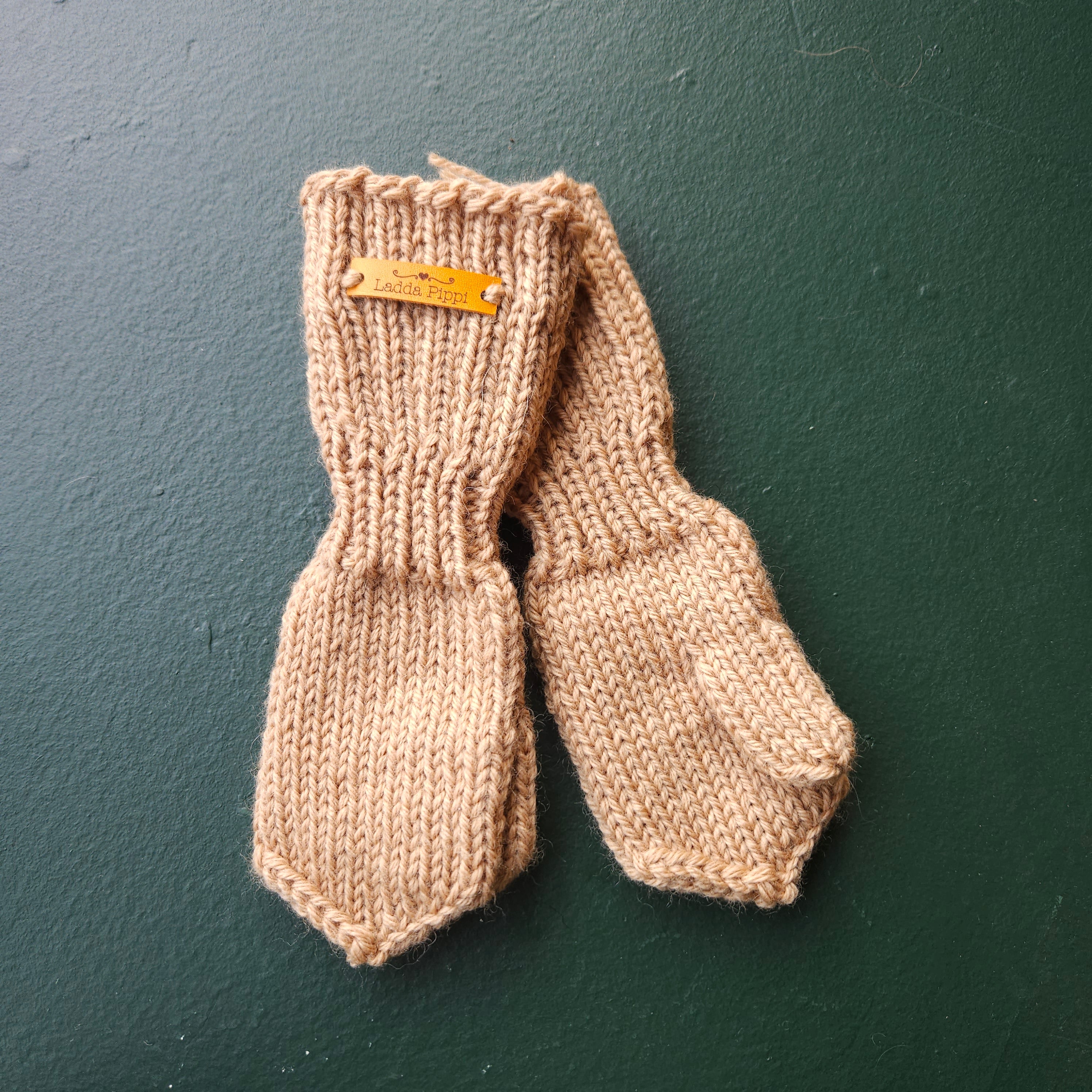 Pair of beige knitted mittens with a brand tag on a dark green background