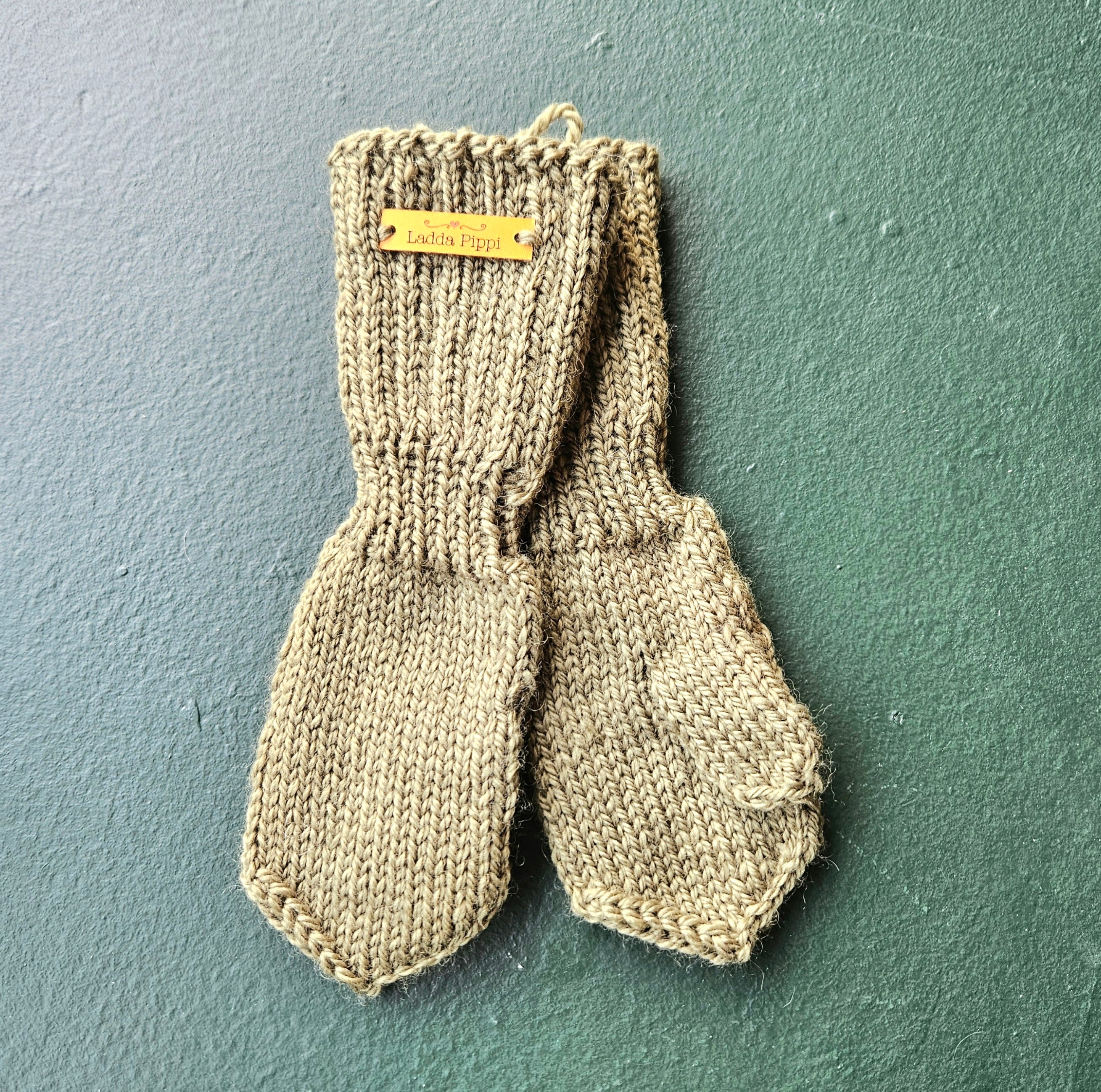 Pair of green knitted baby mittens with a label on a green background