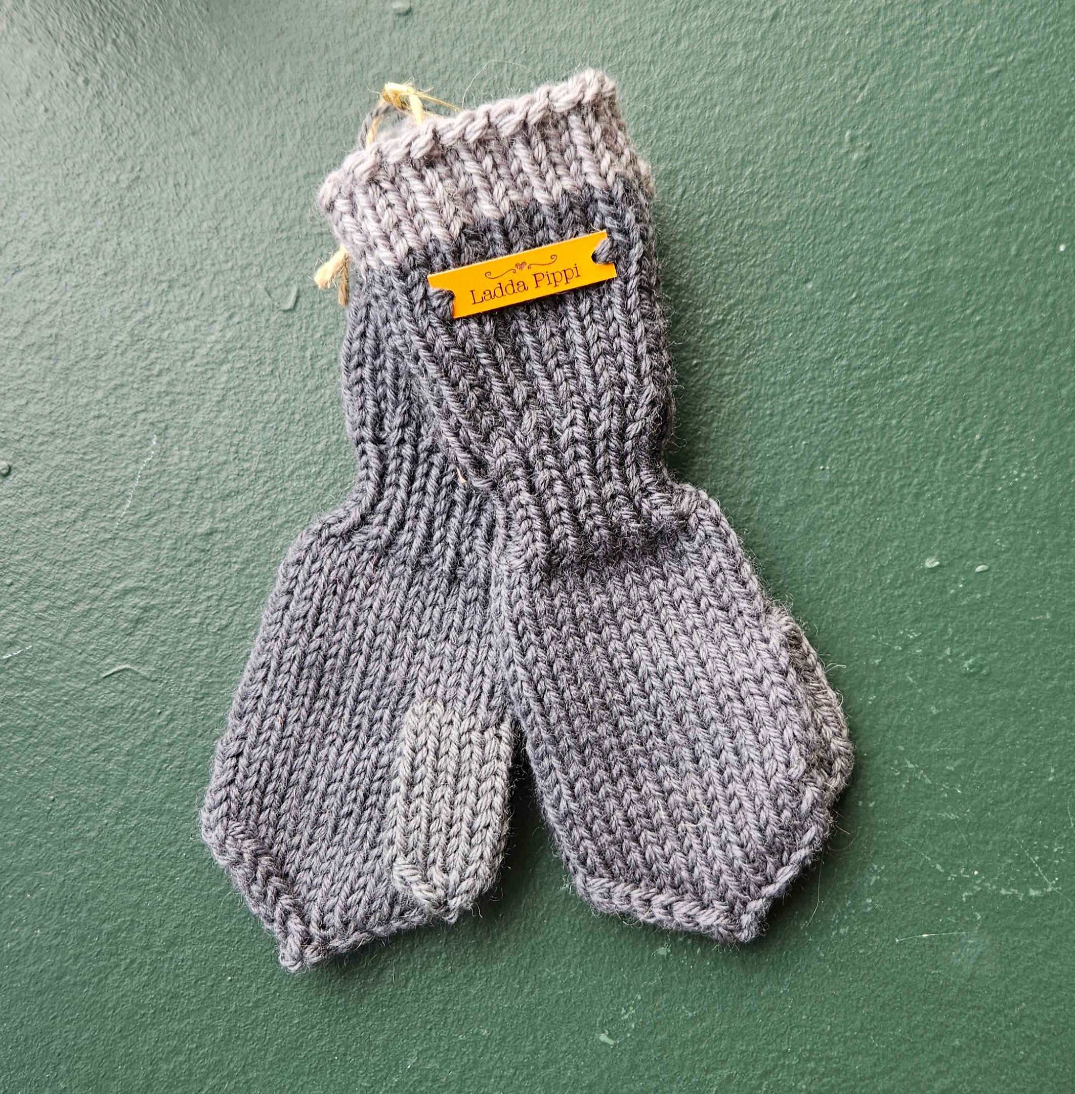 Pair of blue knitted baby mittens with a yellow label on a green background