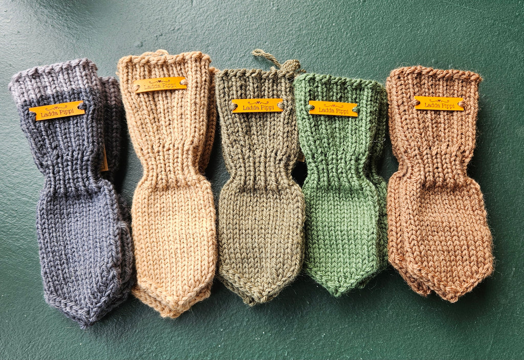 Five pairs of knitted baby mittens in different colors on a green background