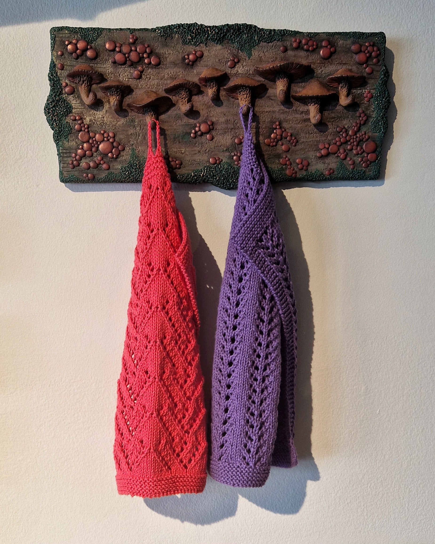 Decorative wall hook with red and purple knitted kitchen towels hanging on a white background