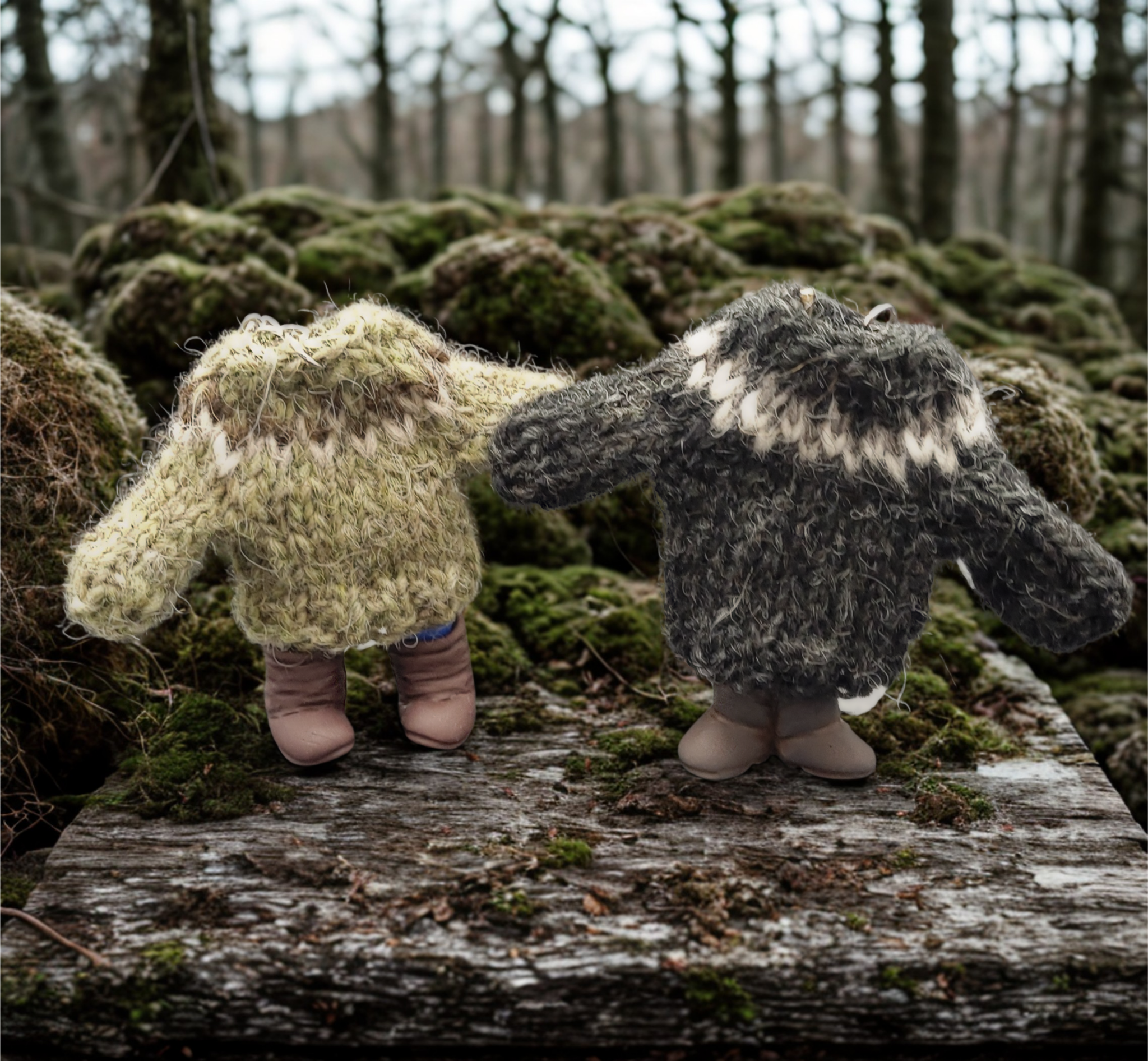 Two knitted wool sweater figures standing on a log in a forest setting.