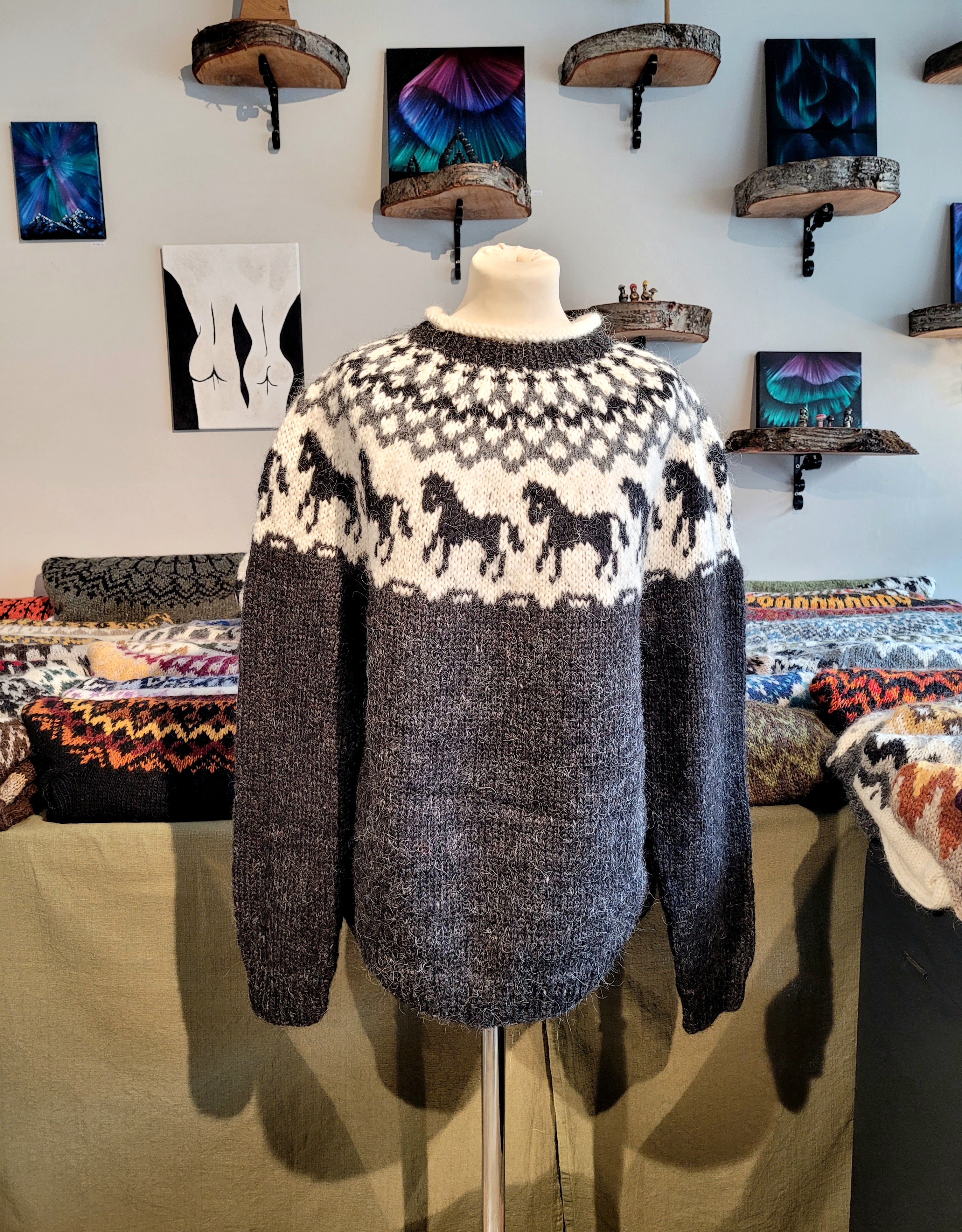 A mannequin in a blue hand-knit Icelandic wool sweater featuring a traditional Nordic pattern in white and light blue colors with black horses in a store setting.