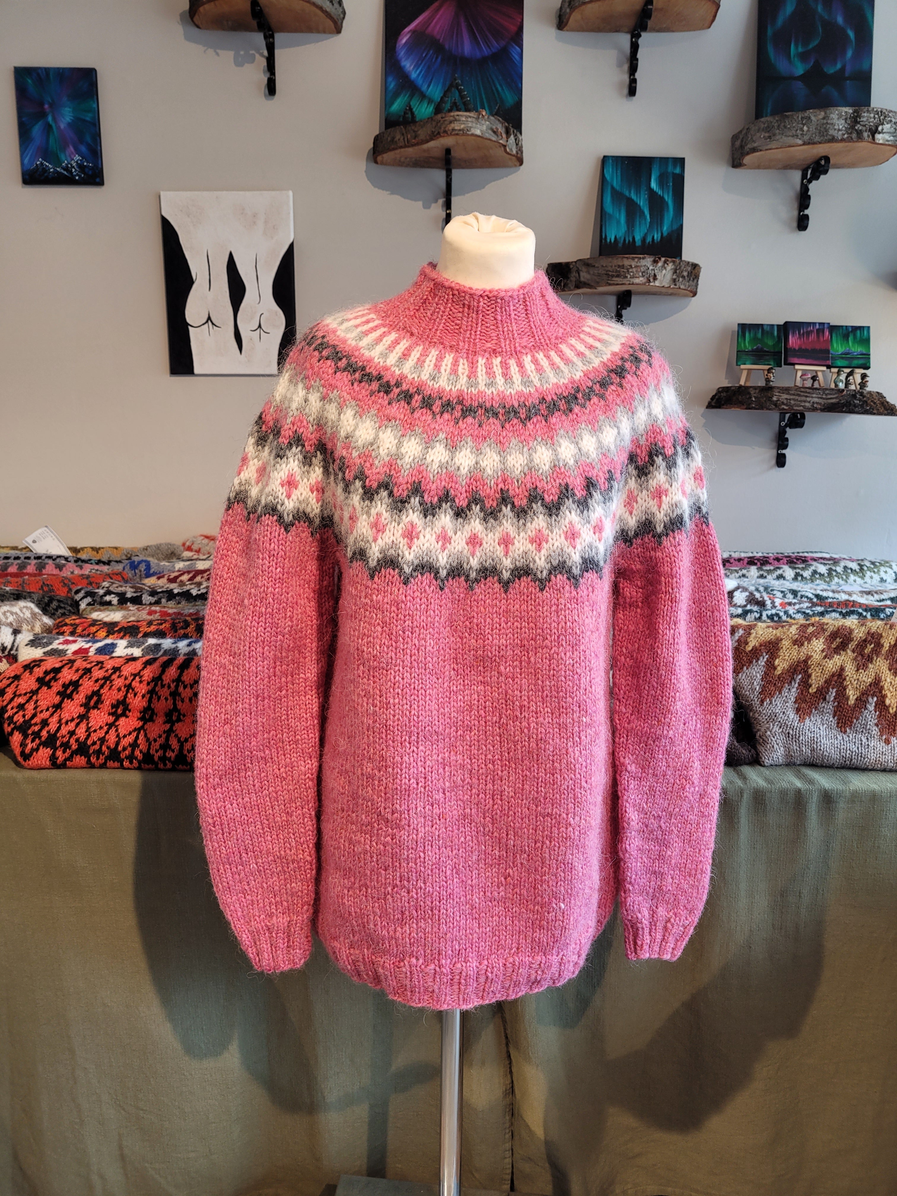 A mannequin in a pink hand-knit Icelandic wool sweater featuring a traditional Nordic pattern in a store setting.