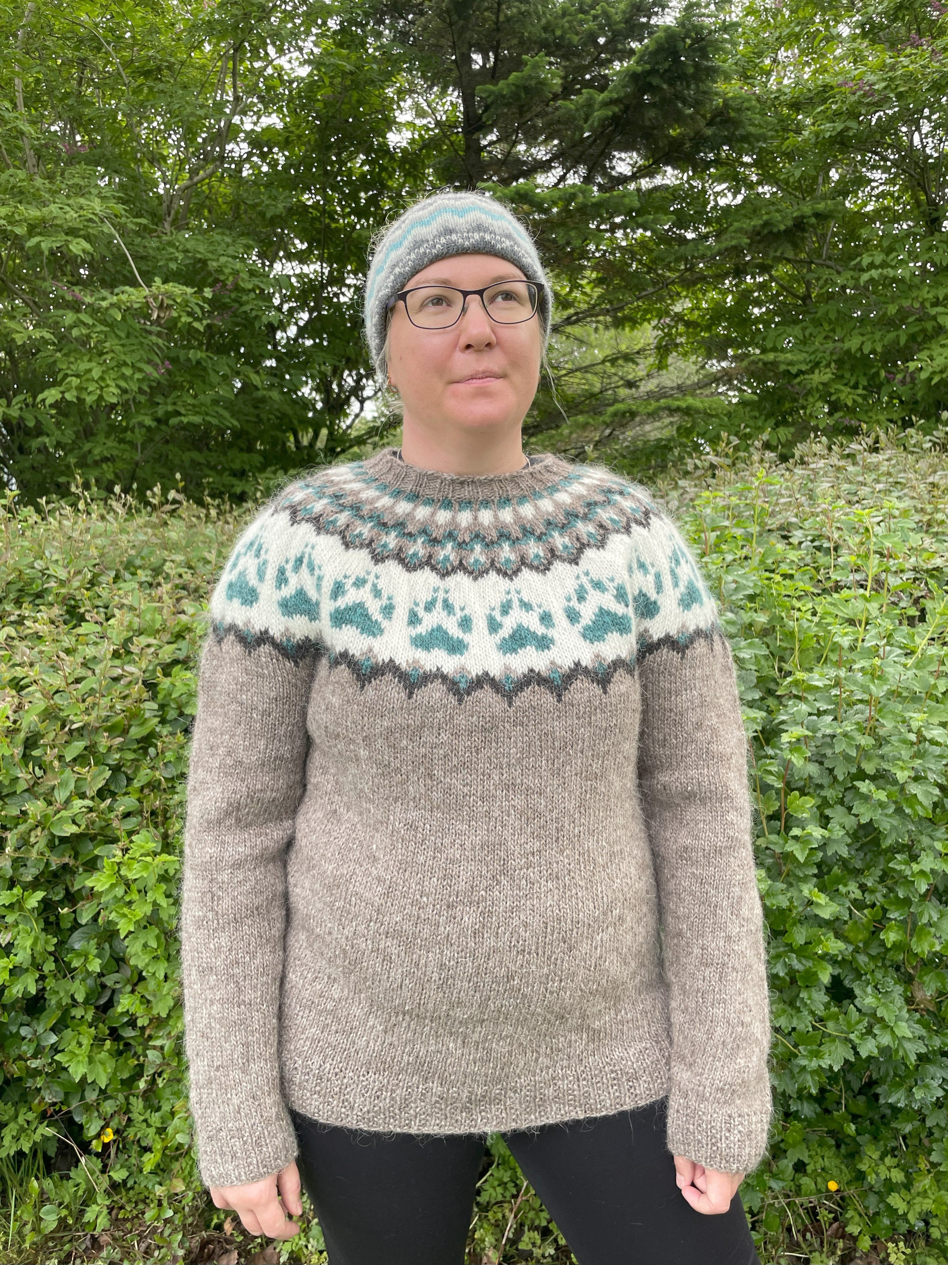 Person wearing a Nordic patterned Icelandic wool sweater and hat outdoors with greenery in the background