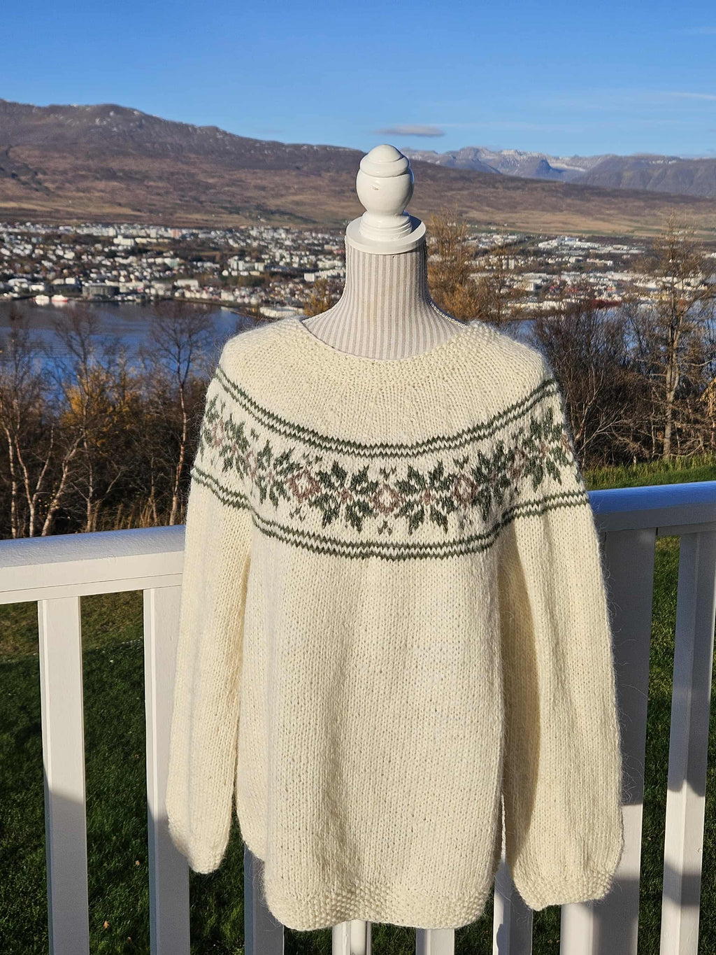 Knitted sweater on a mannequin with a scenic background of mountains and water.