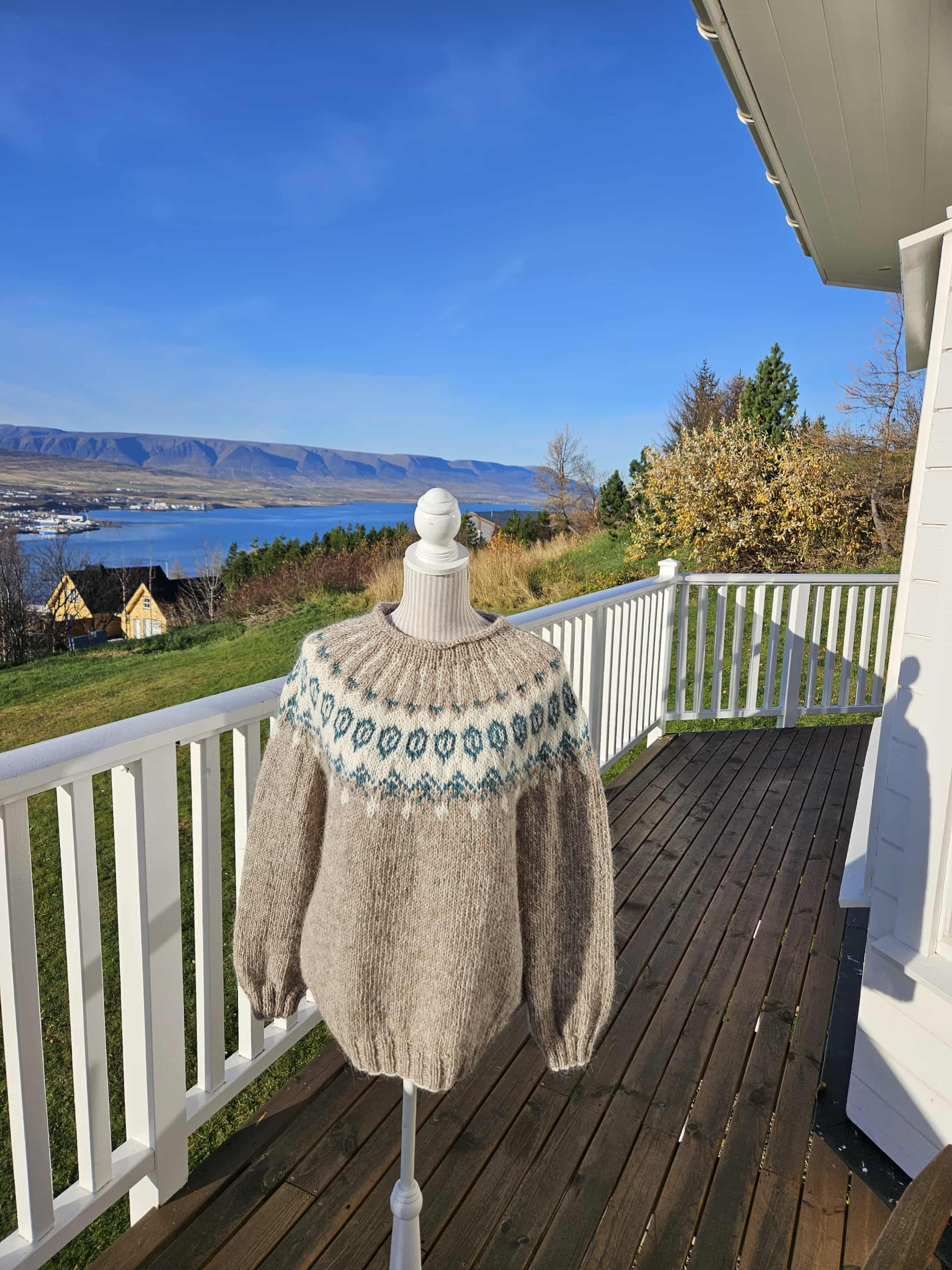 Knitted sweater on a mannequin against a scenic backdrop of a lake and mountains.