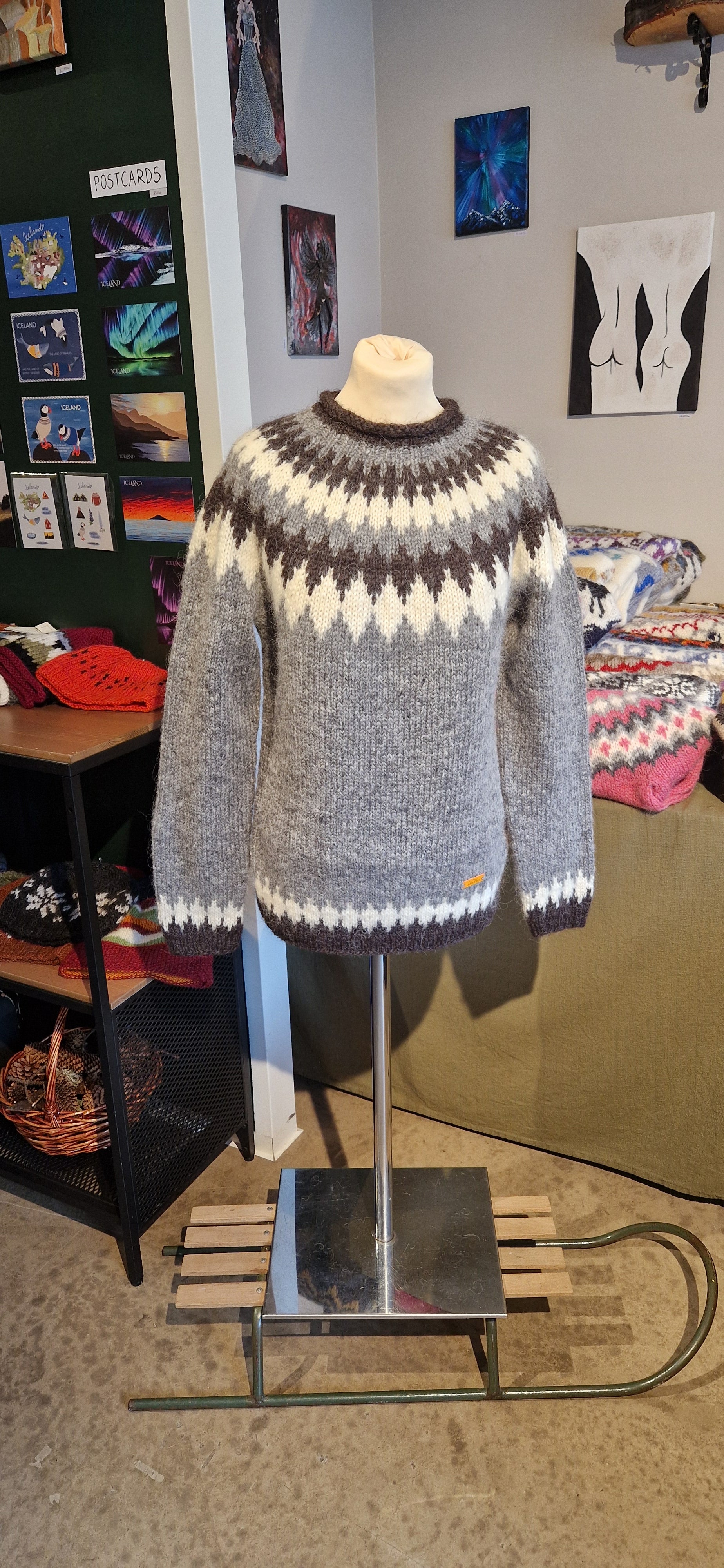 A mannequin in a gray hand-knit Icelandic wool sweater featuring a traditional Nordic pattern in white and black colors in a store setting.