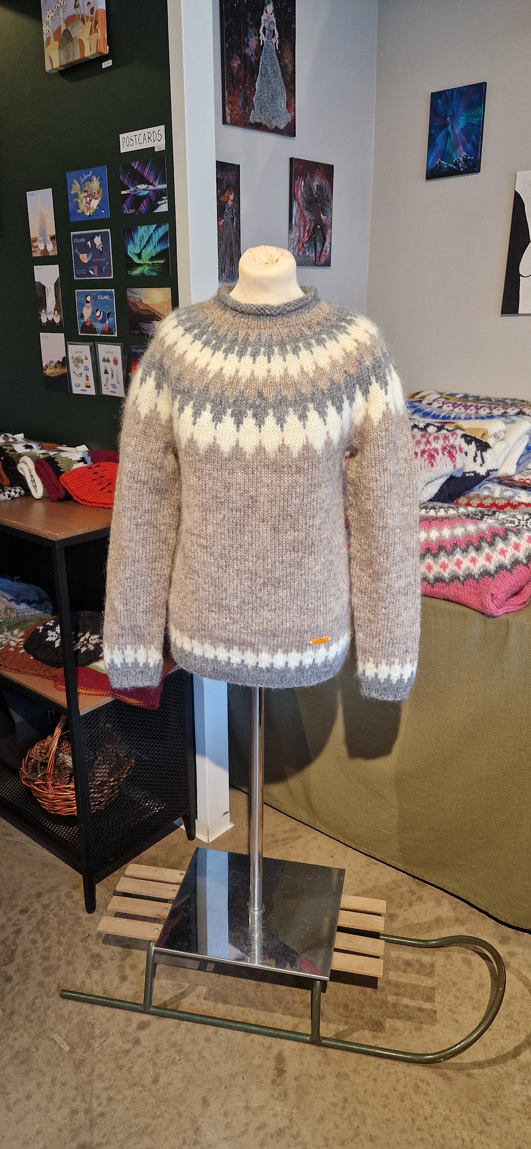 A mannequin in a beige hand-knit Icelandic wool sweater featuring a traditional Nordic pattern in white and gray in a store setting.