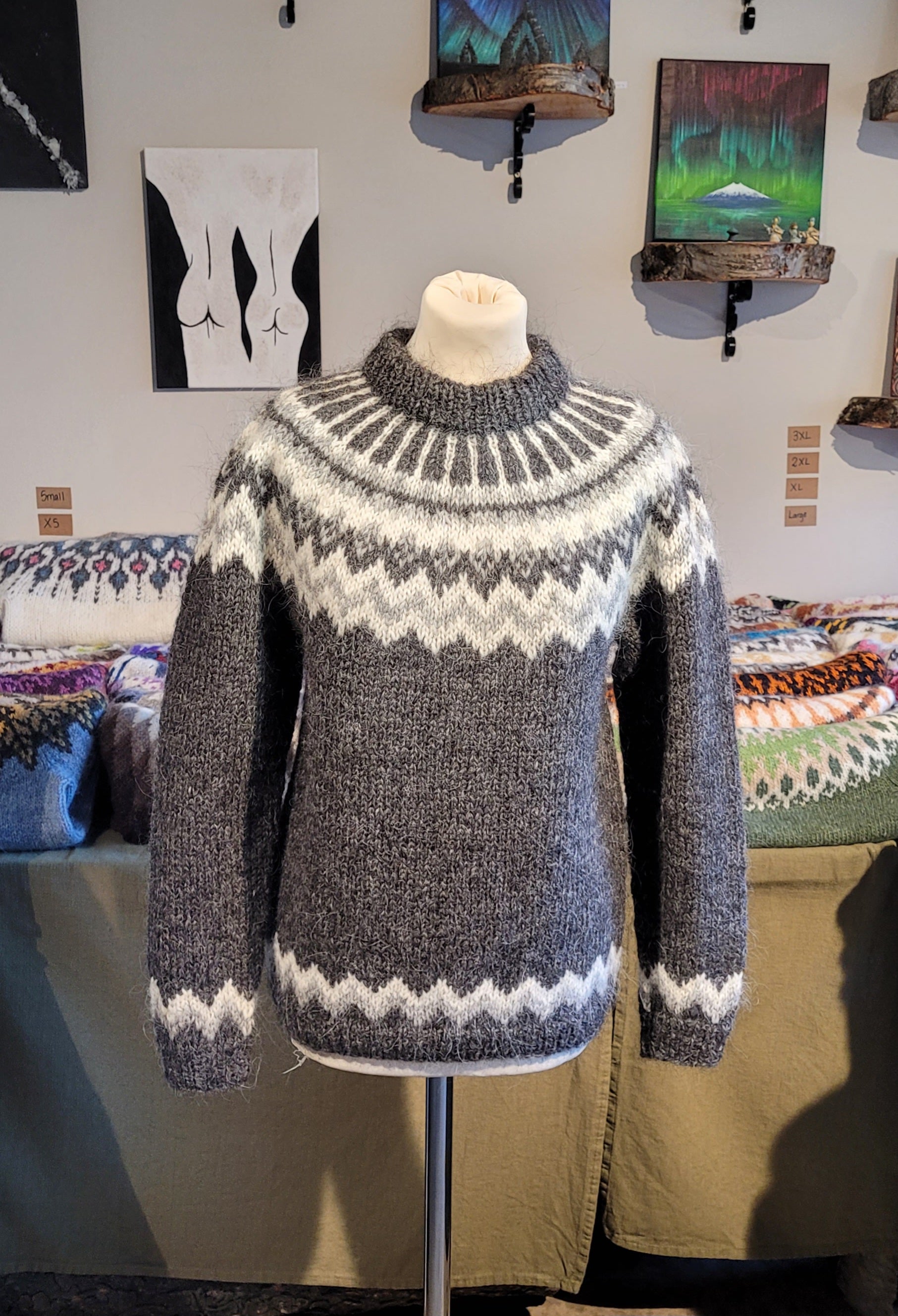Gray and white patterned sweater on a mannequin against a wall with artwork.