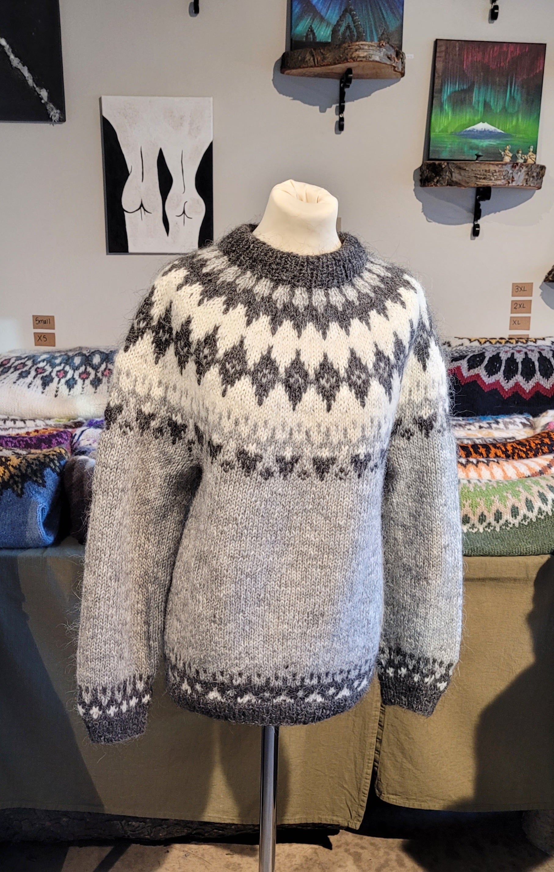 Knitted sweater on a mannequin against a wall with art and fabric in the background