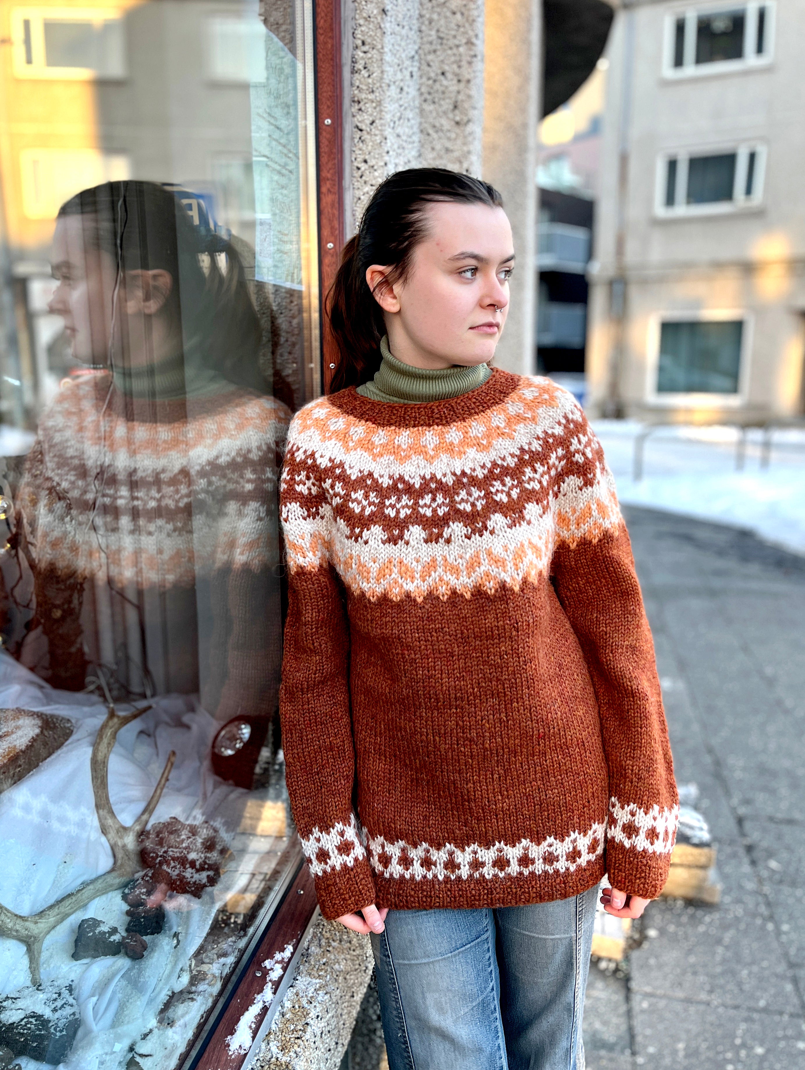 A woman in a hand knit Icelandic wool sweater featuring a traditional Nordic pattern in brown, white, and beige colors.