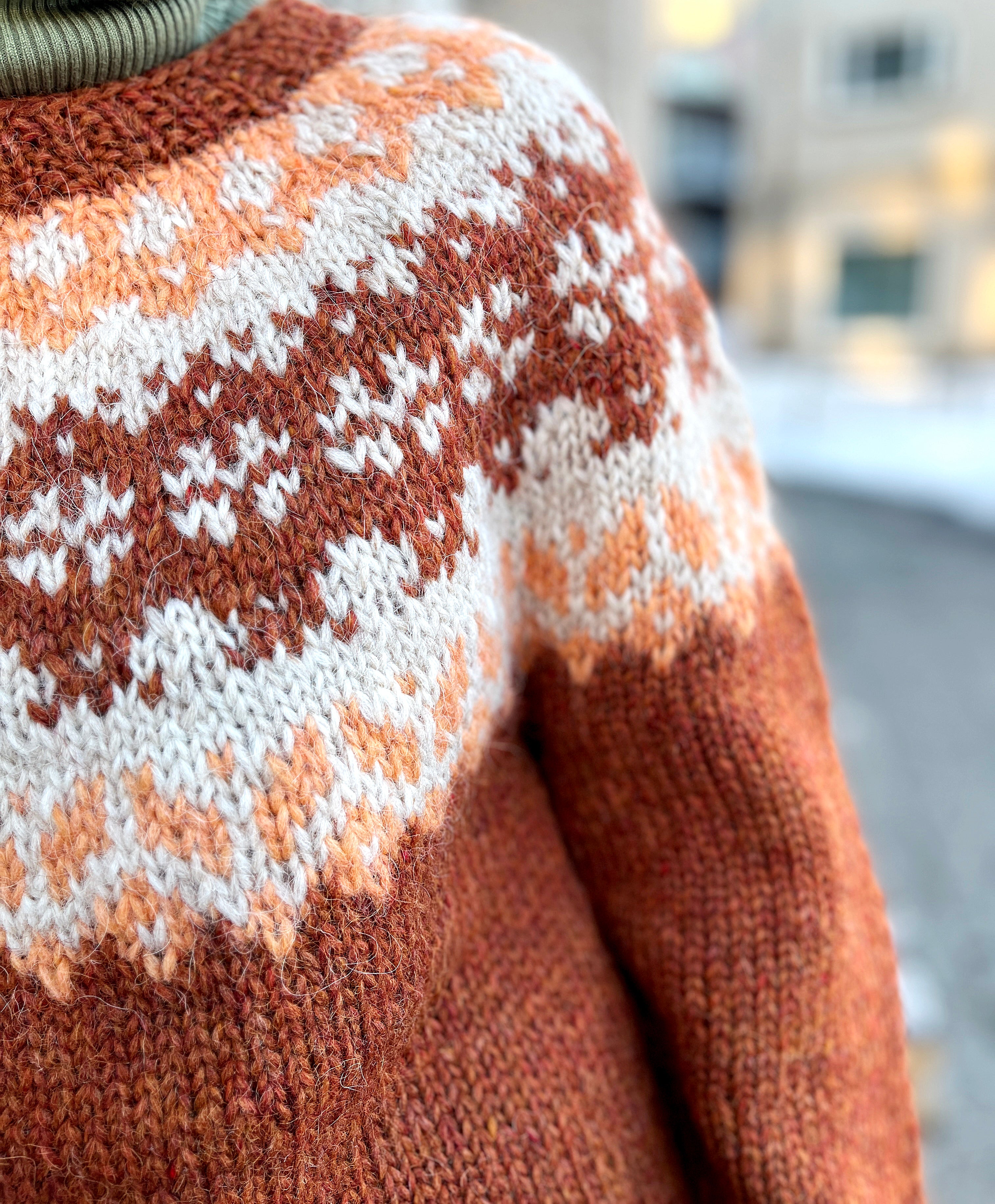 Close-up of a hand knit Icelandic wool sweater featuring a traditional Nordic pattern in brown, white, and beige colors.