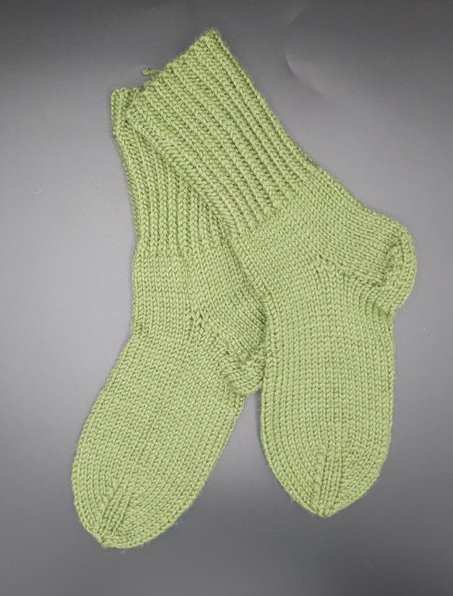 Pair of green knitted socks on a gray background
