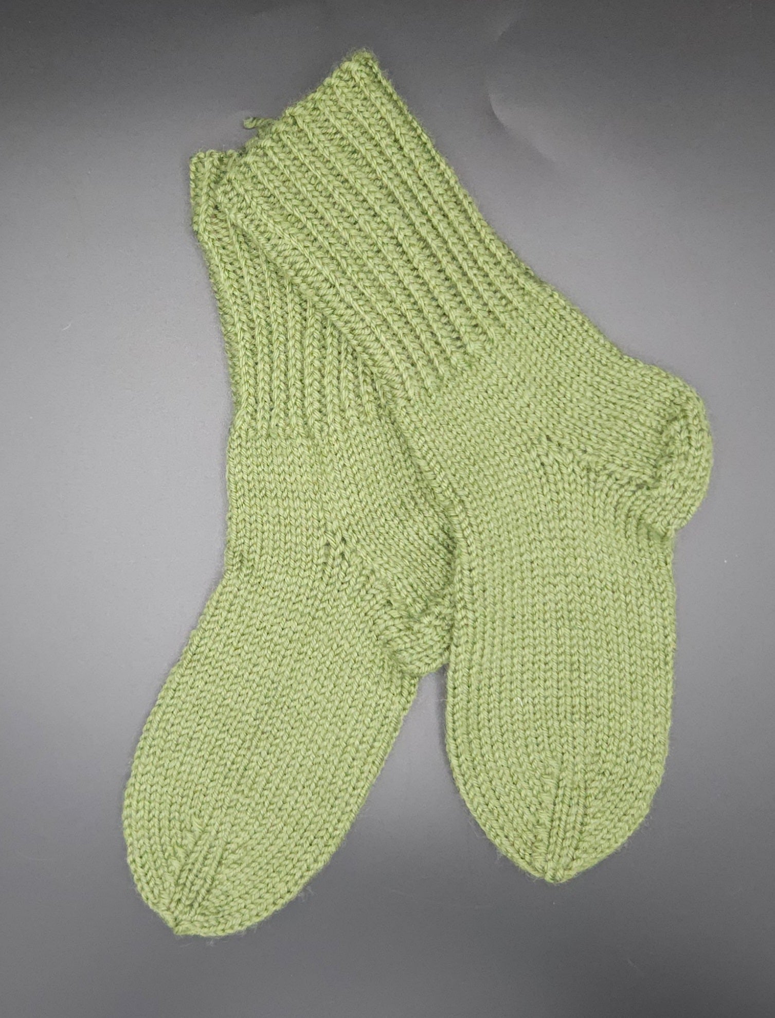Pair of green knitted socks on a gray background