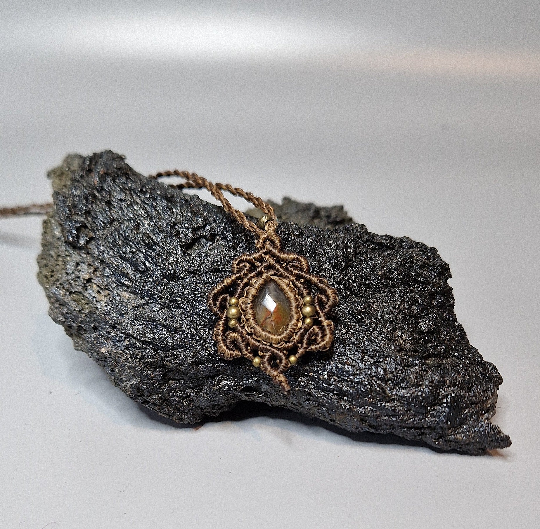 Brown necklace with a pendant and a central stone on a dark rock against a light background