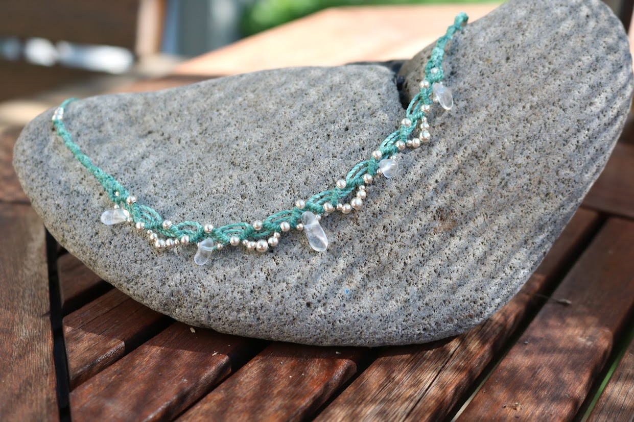 Necklace with green and white beads and clear quartz stones on a gray stone
