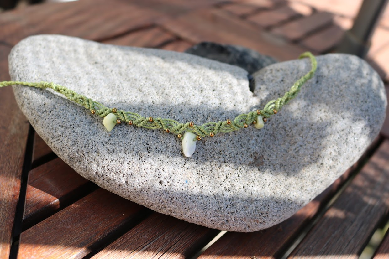 Green braided necklace with white stones on a stone surface
