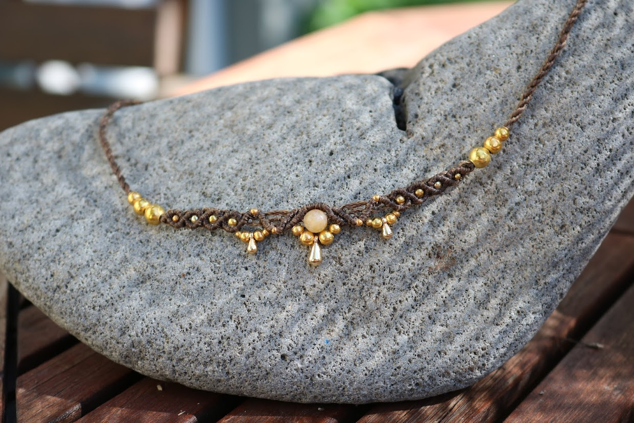 Necklace with gold beads and a central stone on a gray stone surface