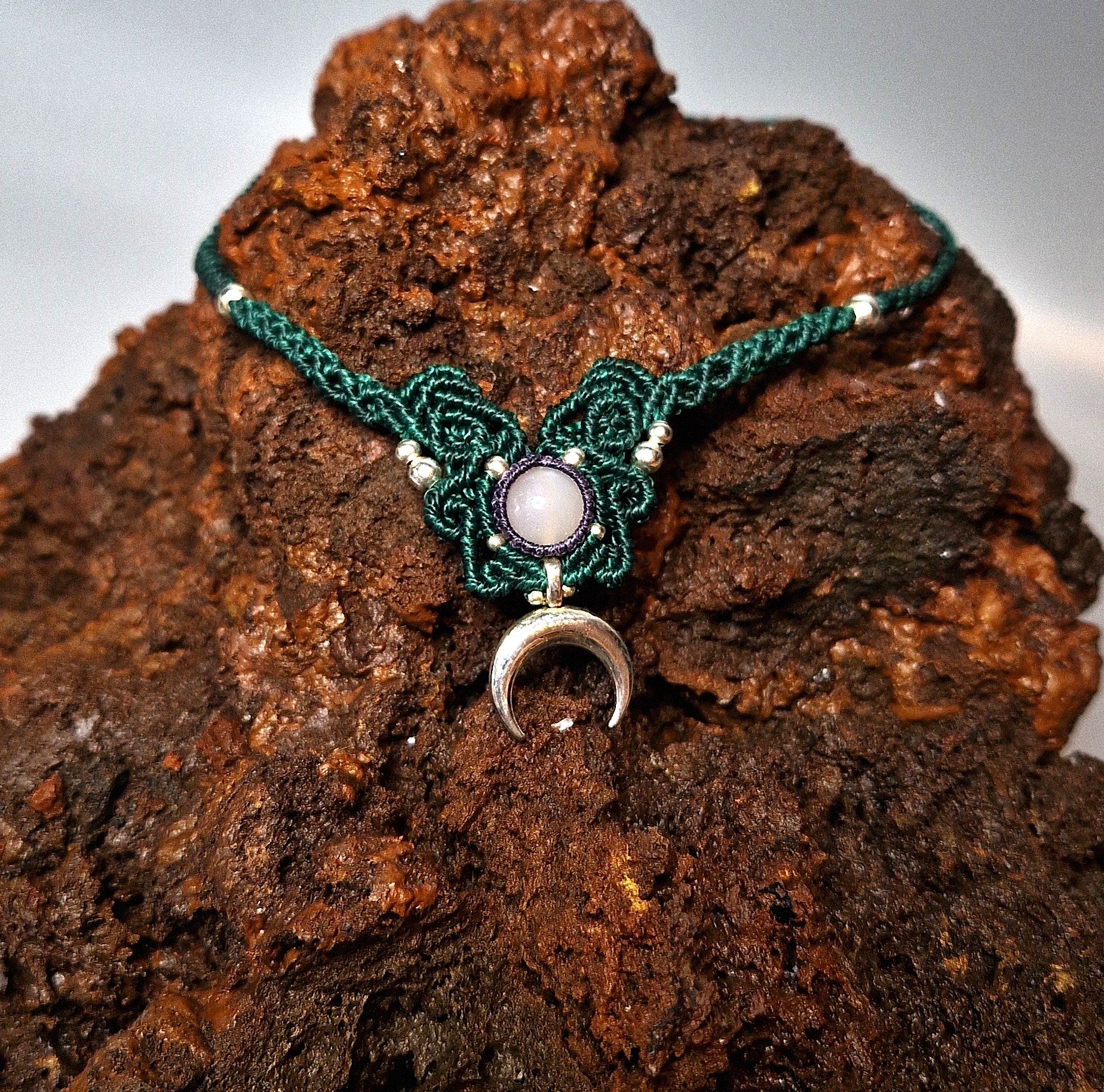 Green macrame necklace with a moon pendant on a textured brown surface