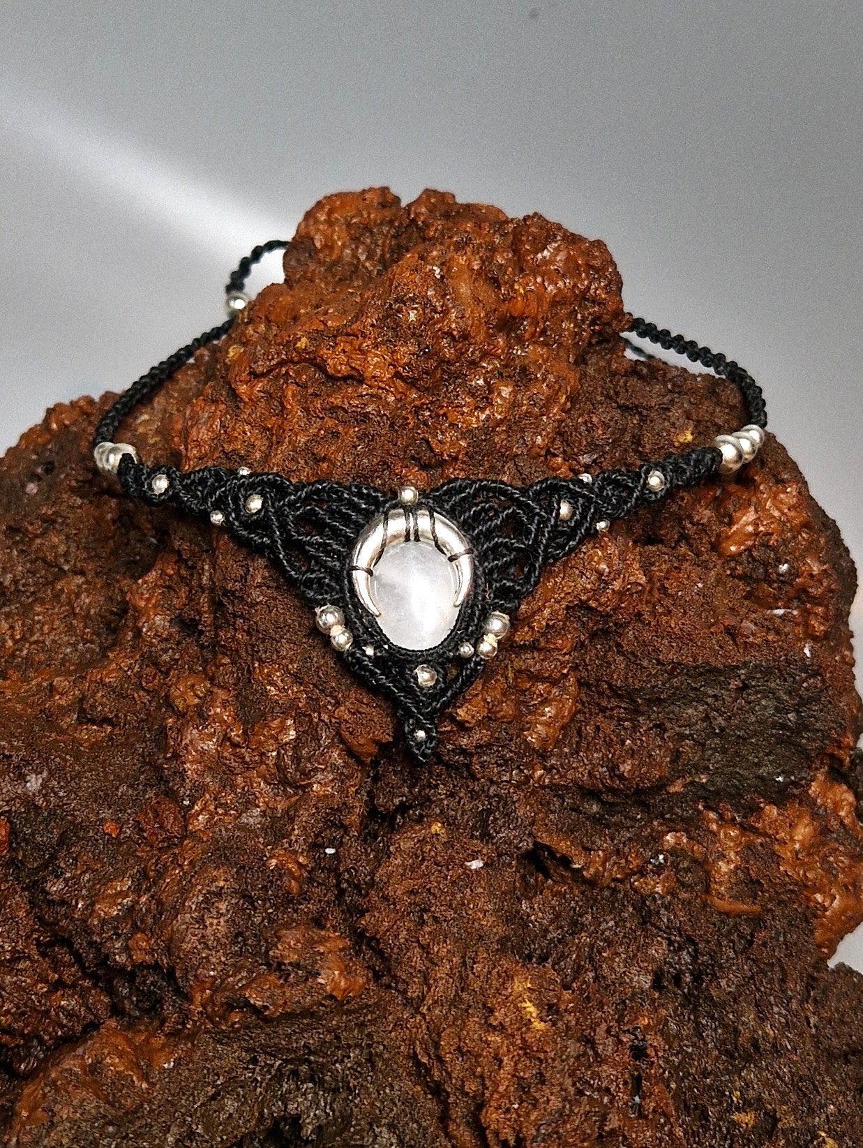Black lace necklace with a white stone pendant on a textured brown surface
